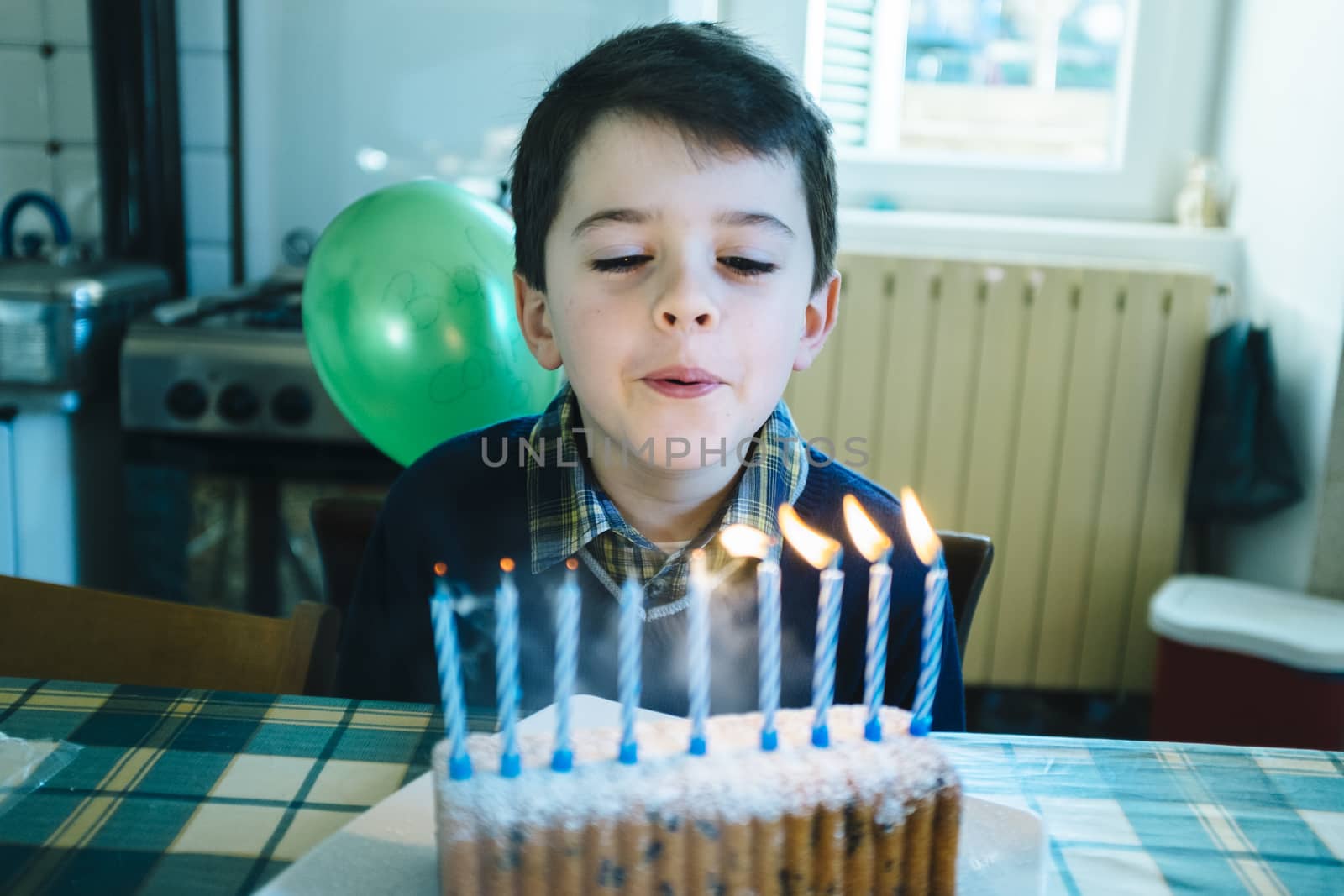 baby in the day of his ninth birthday blowing the candles on the cake, in the kitchen of his home