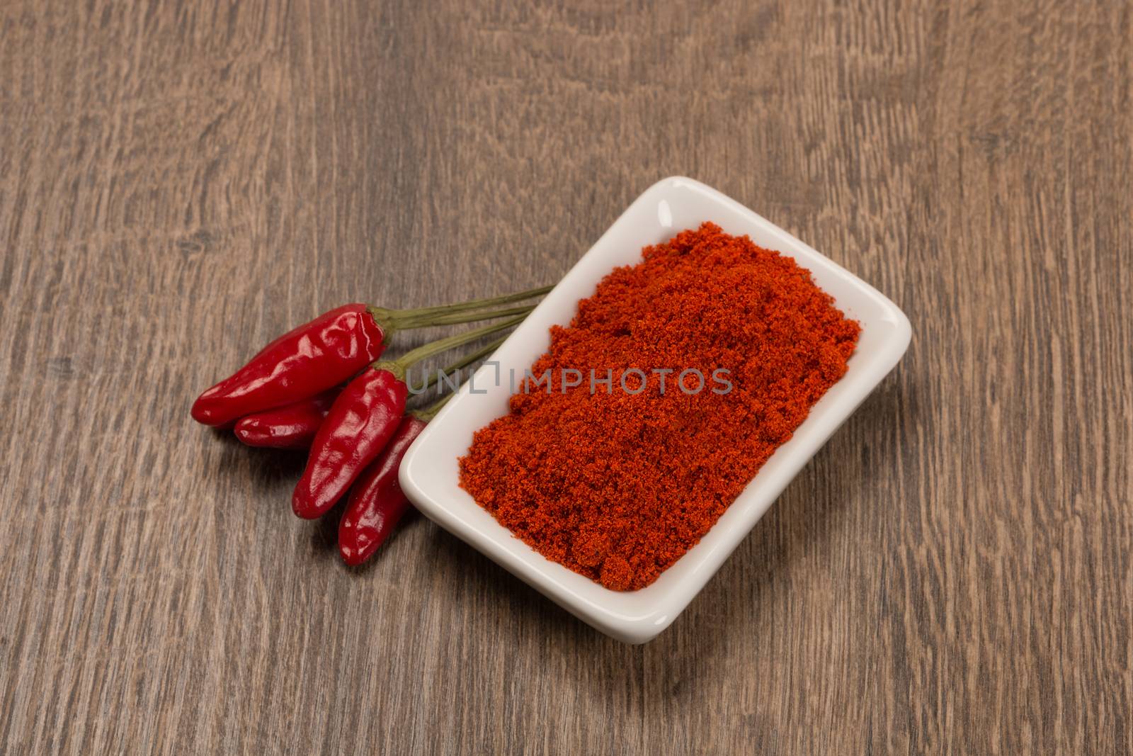 Red chili pepper with chili powder over wood.