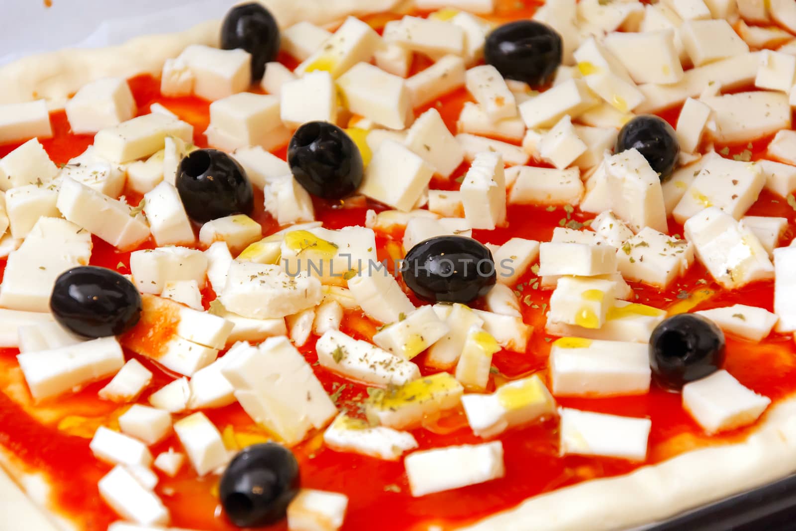 Raw pizza decorated mozzarella, black olives and tomato sauce ready to be baked