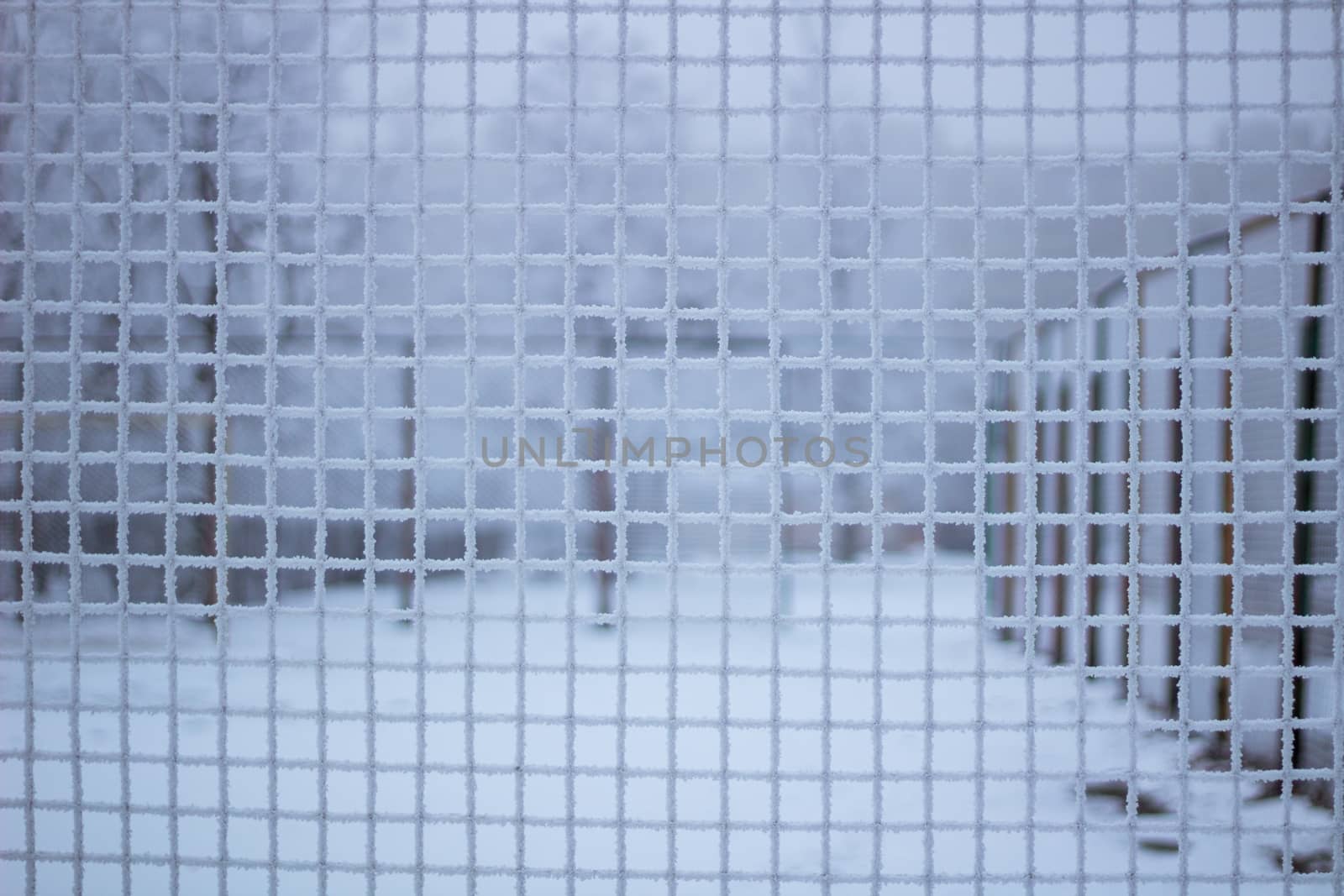 Snowed sport yard behind frosty metal grid net in winter time