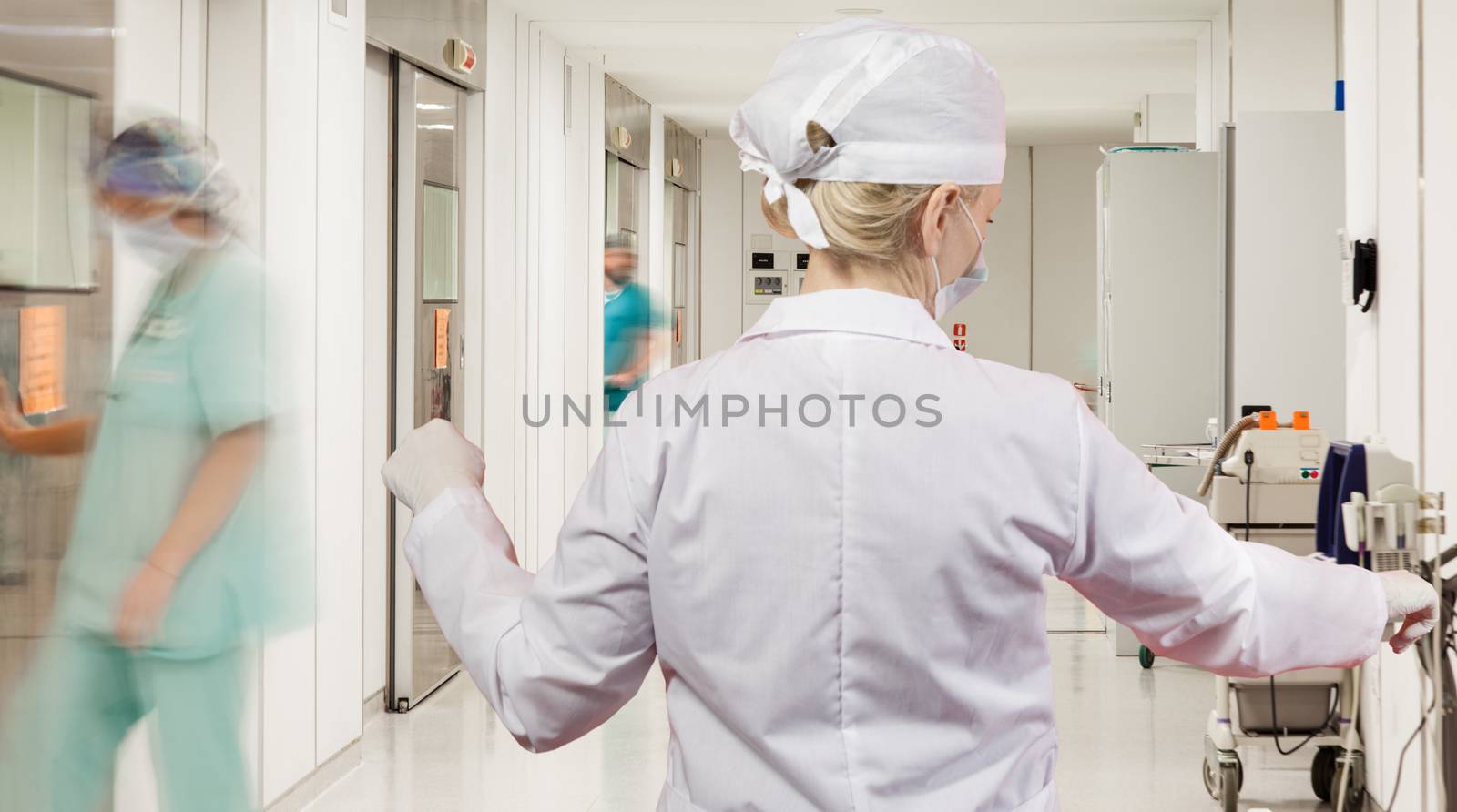 A sterile corridor to operating rooms in modern hospital with female doctor over motion blurred figures of doctors and nurses.