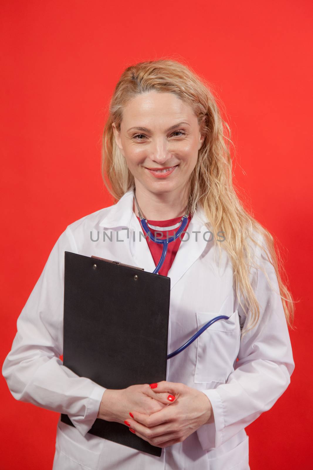 Portrait of young female doctor with white apron and folder on red background.