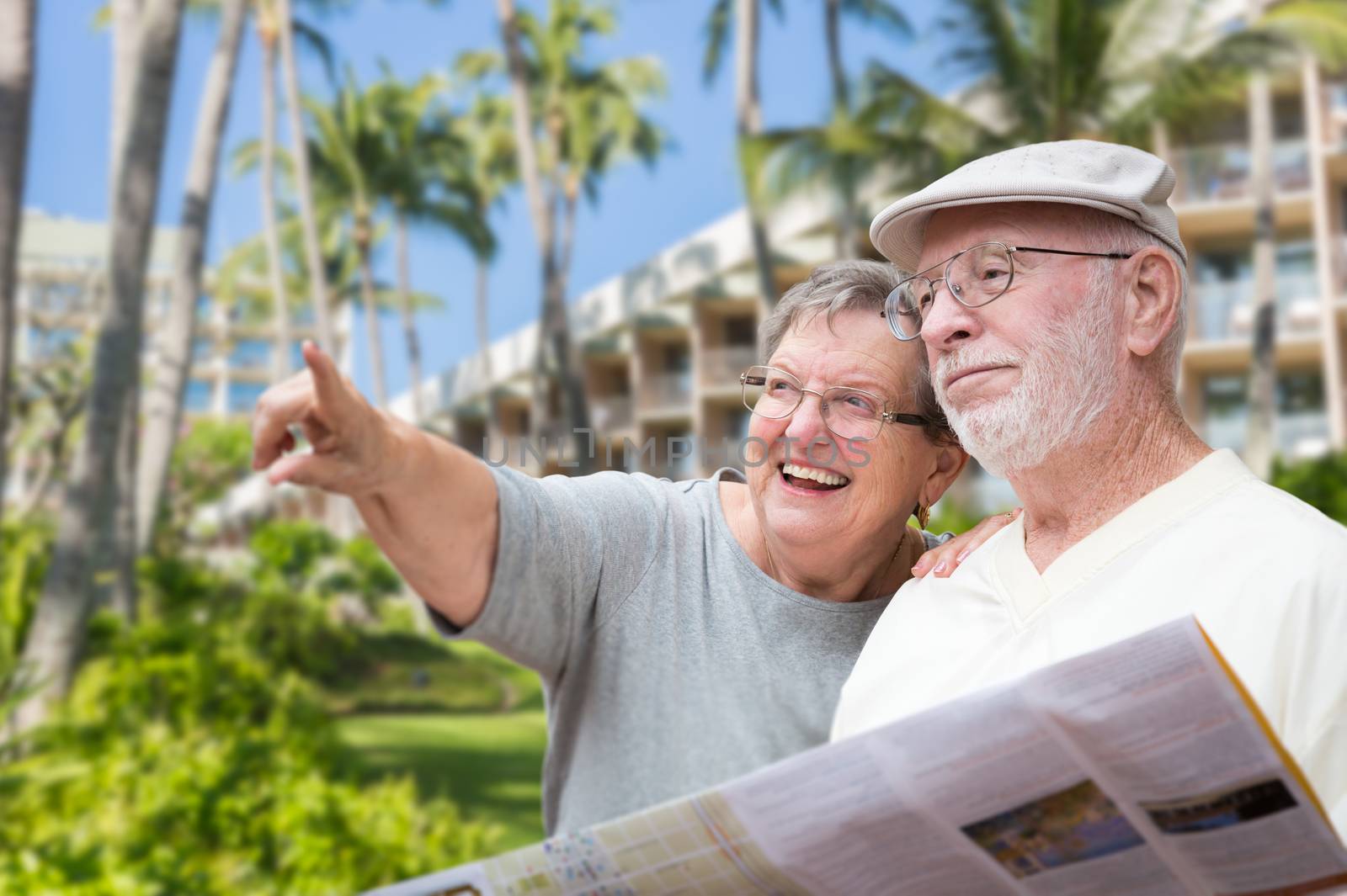 Happy Senior Adult Couple Tourists with Brochure Next To Tropical Hotel and Palm Trees.