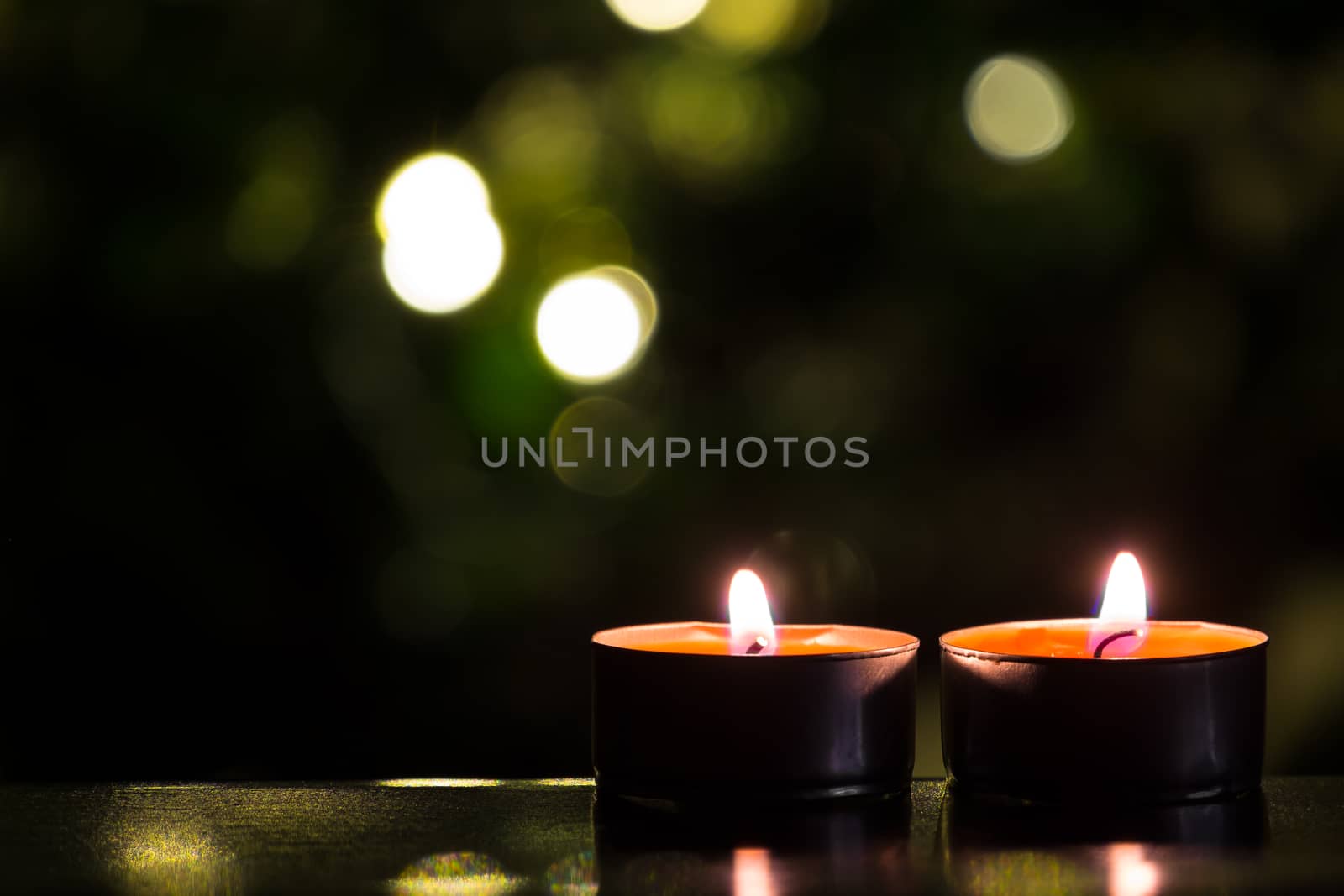 Two candles with christmas tree and lights at the background