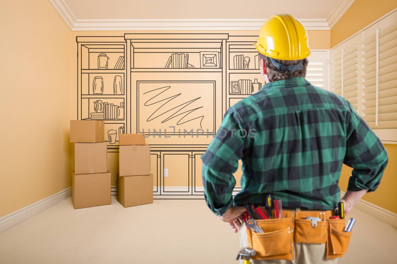 Contractor Standing Indoors with Moving Boxes Looking At Line Drwaing of Entertainment Unit on Wall.