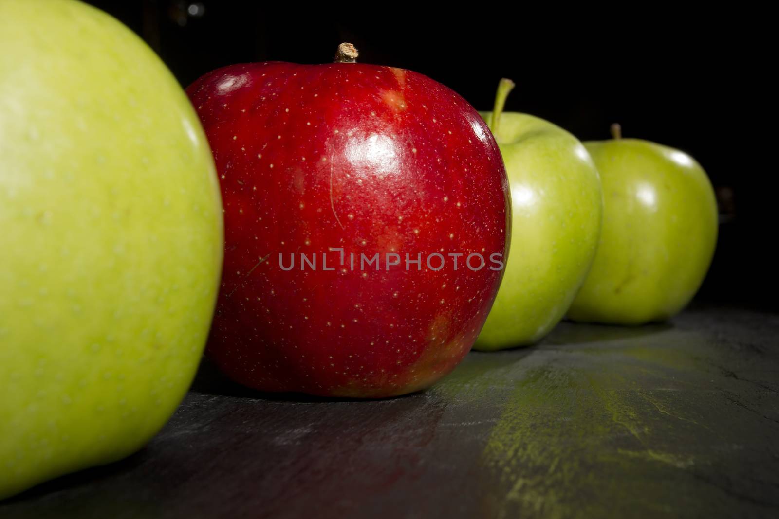 Red apple standing out in a row of green apples