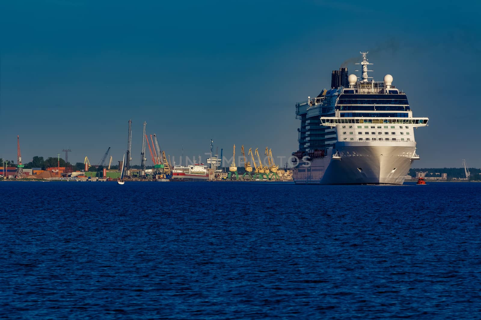 Giant white passenger ship moving past the port on a clear day