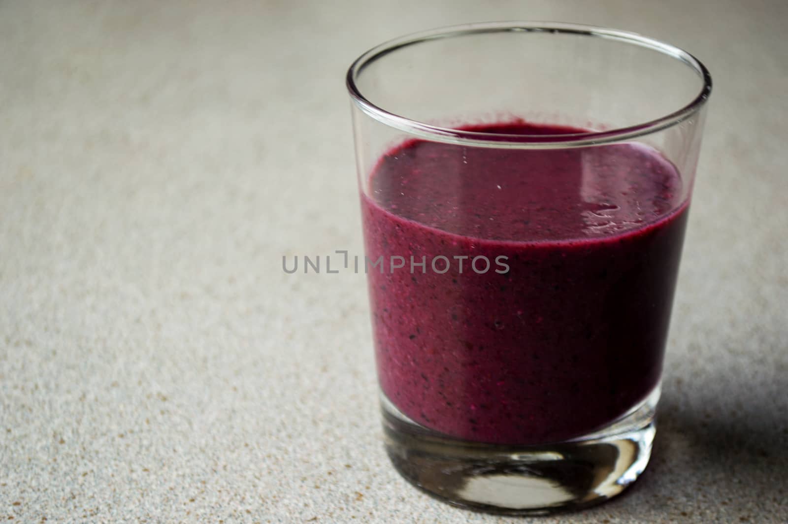 Purple smoothie with berries and fruit in glass on a grey table.