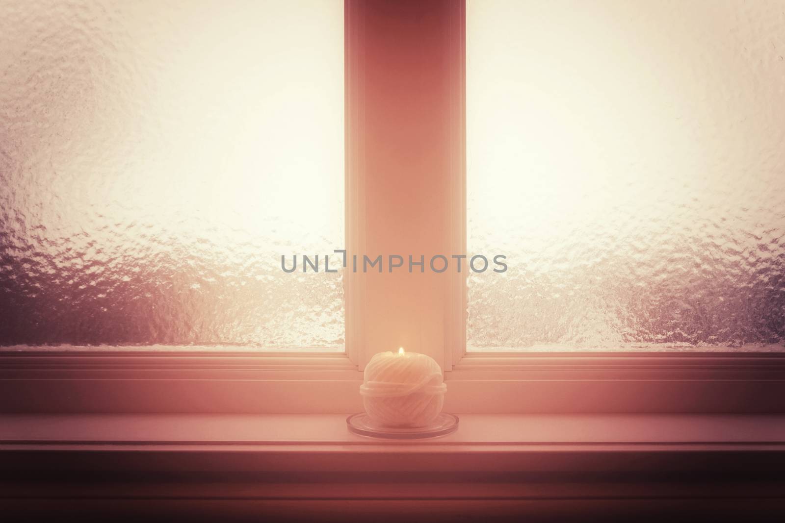 Frosted window and burning candle and in misty light. Winter mood.
