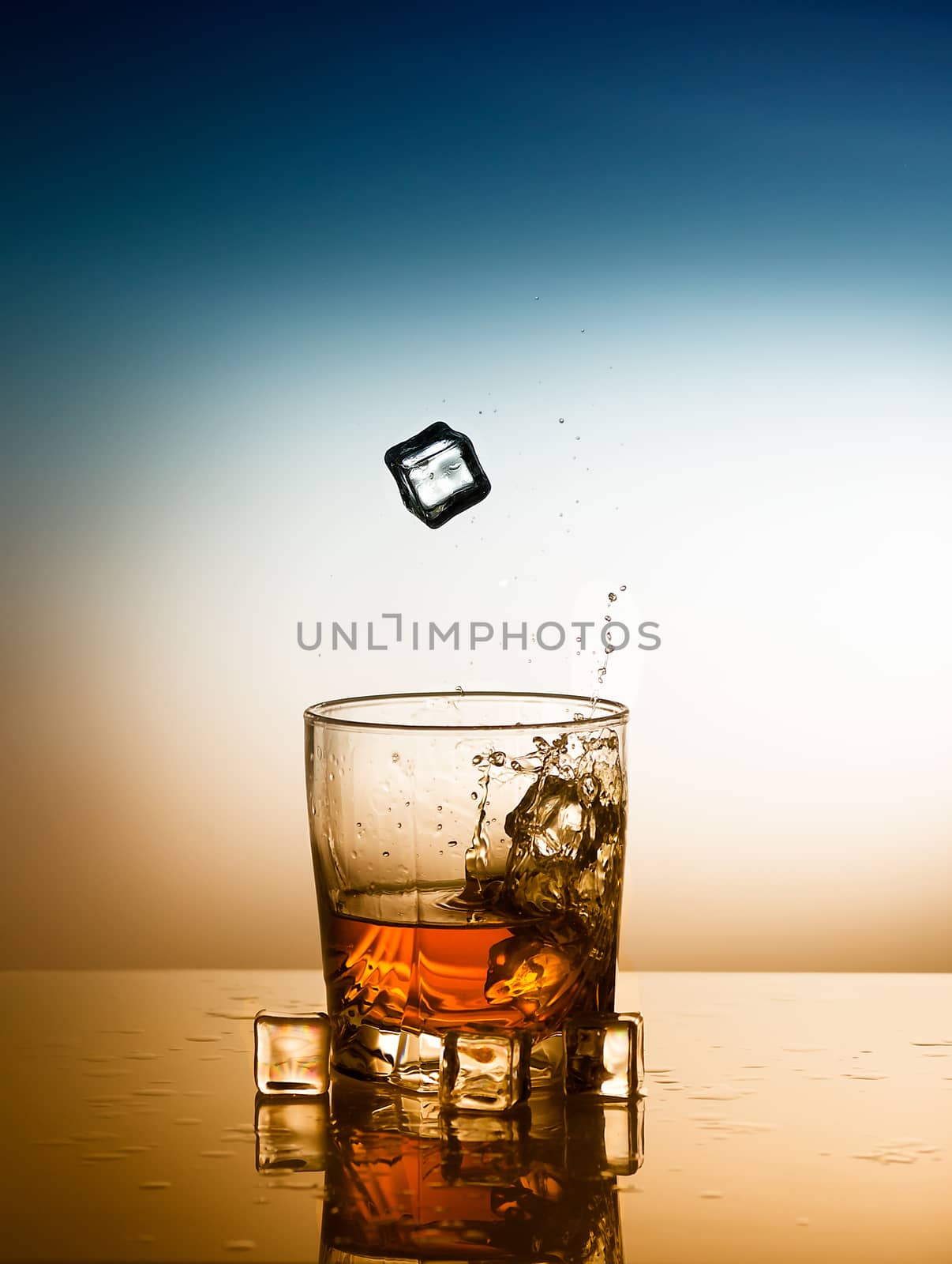 a glass of whiskey with falling ice cubes
