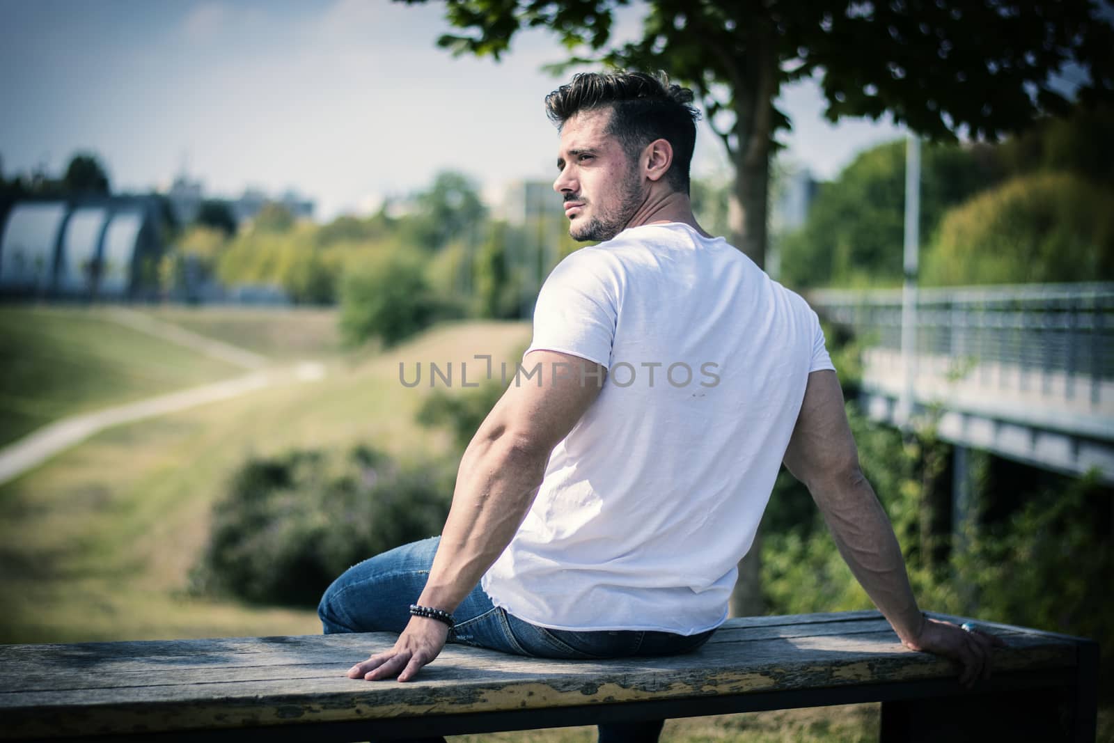 Attractive muscular man in city park in a nice summer day, seen from the back