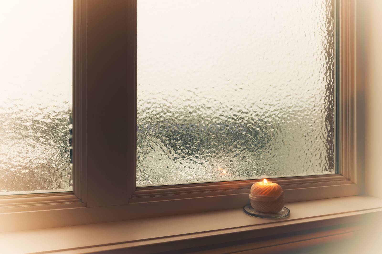 Burning candle and frosted window in hazy light. Winter composition.