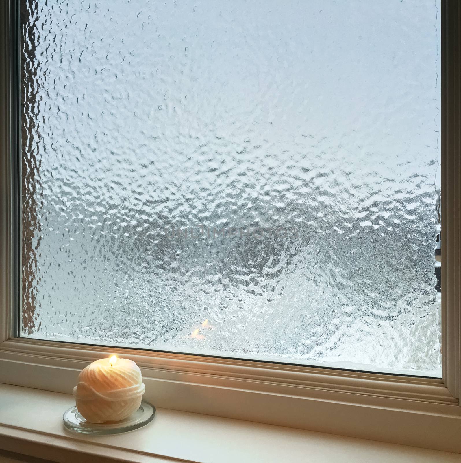 Candle burning near frosted window. Weather after freezing rain.