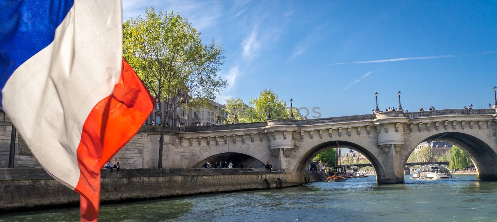 Cruising on a peniche boat in Paris in spring, with a bridge and french flag in the foreground