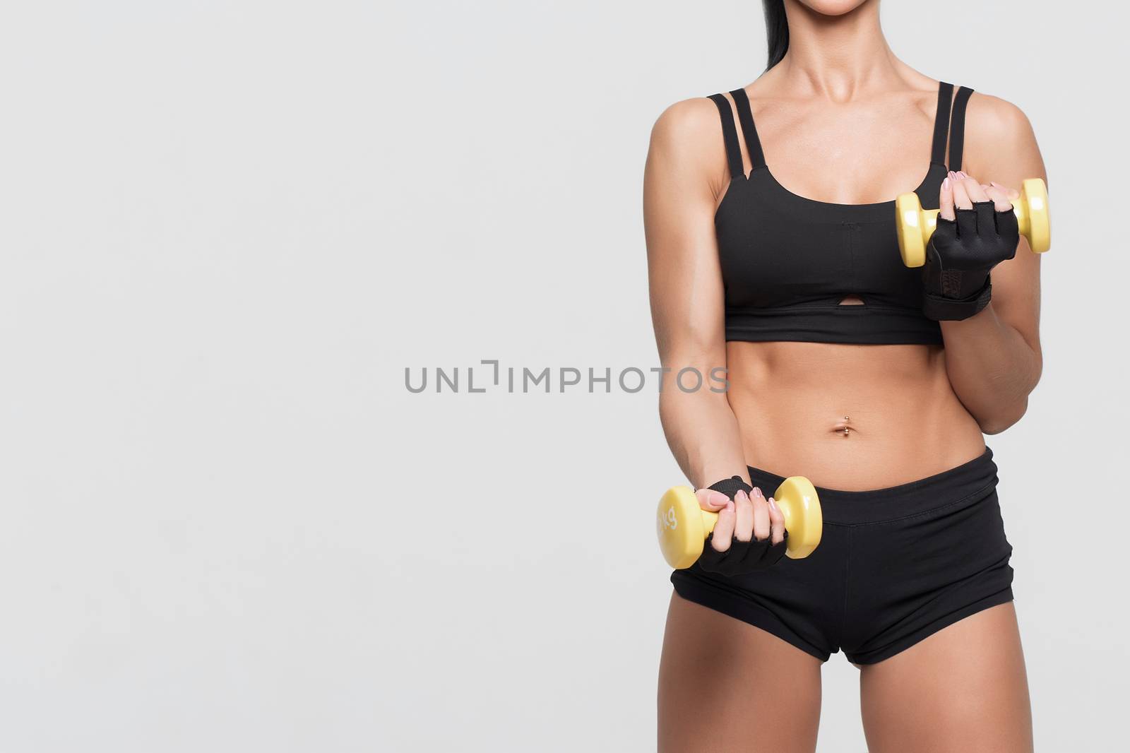 Girl bodybuilder on a gray background with dumbbells in hands