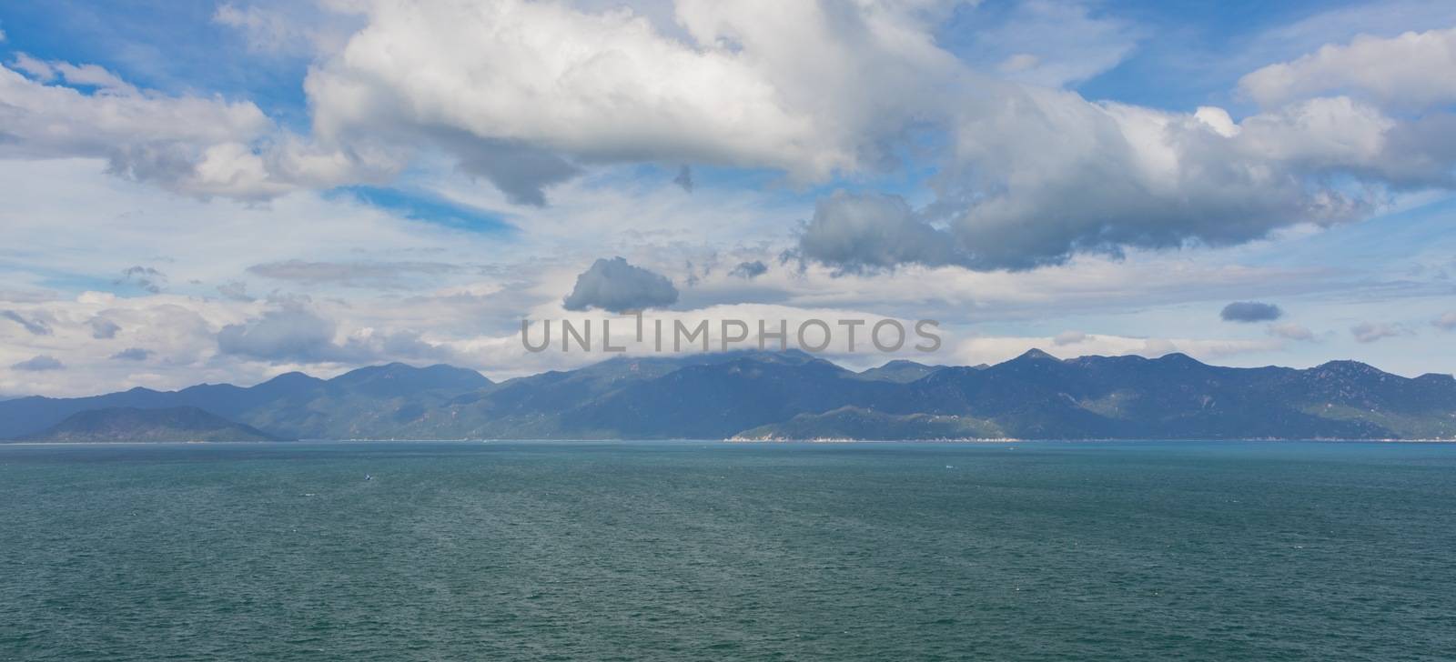 Ocean waves lapping across the south china sea in central Vietnam with a mountain range and cloudy dramatic skies.