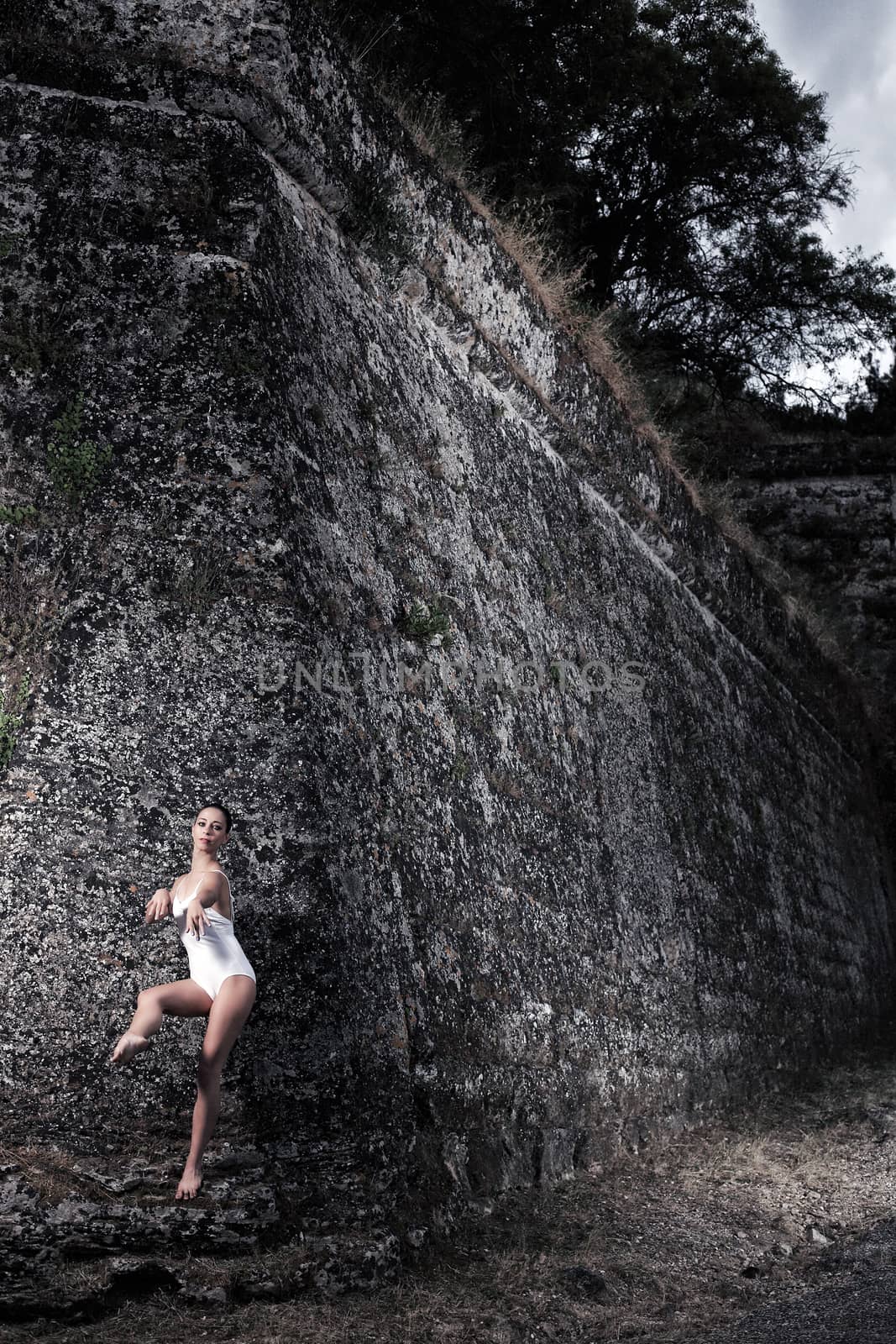 portrait of a beautiful young ballerina posing in front of a big wall of an old castle