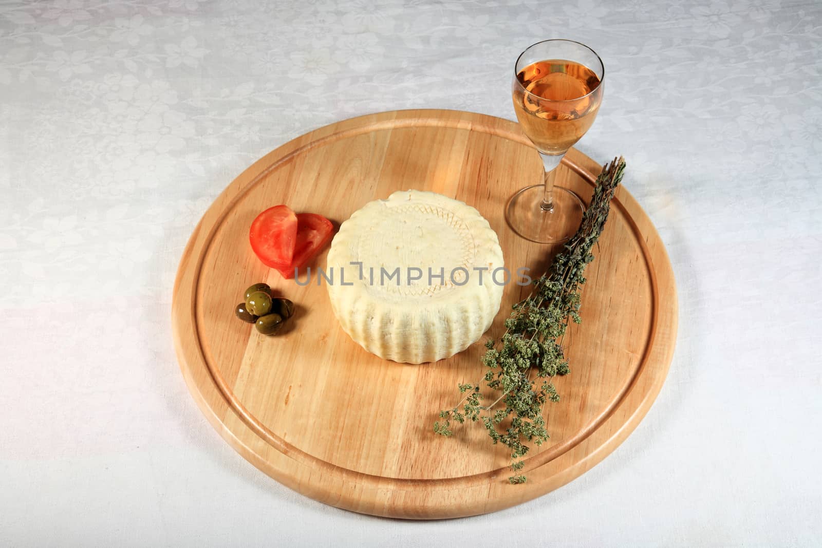 block of spicy cheese with oregano and tomato with olives on wooden plate