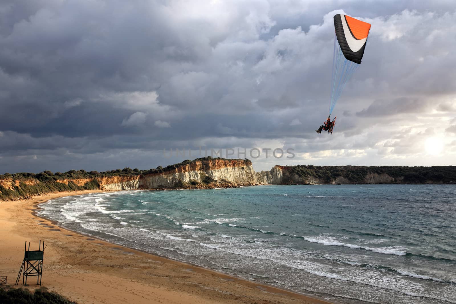 paraglider flying above a beautiful beach in a cloudy day
