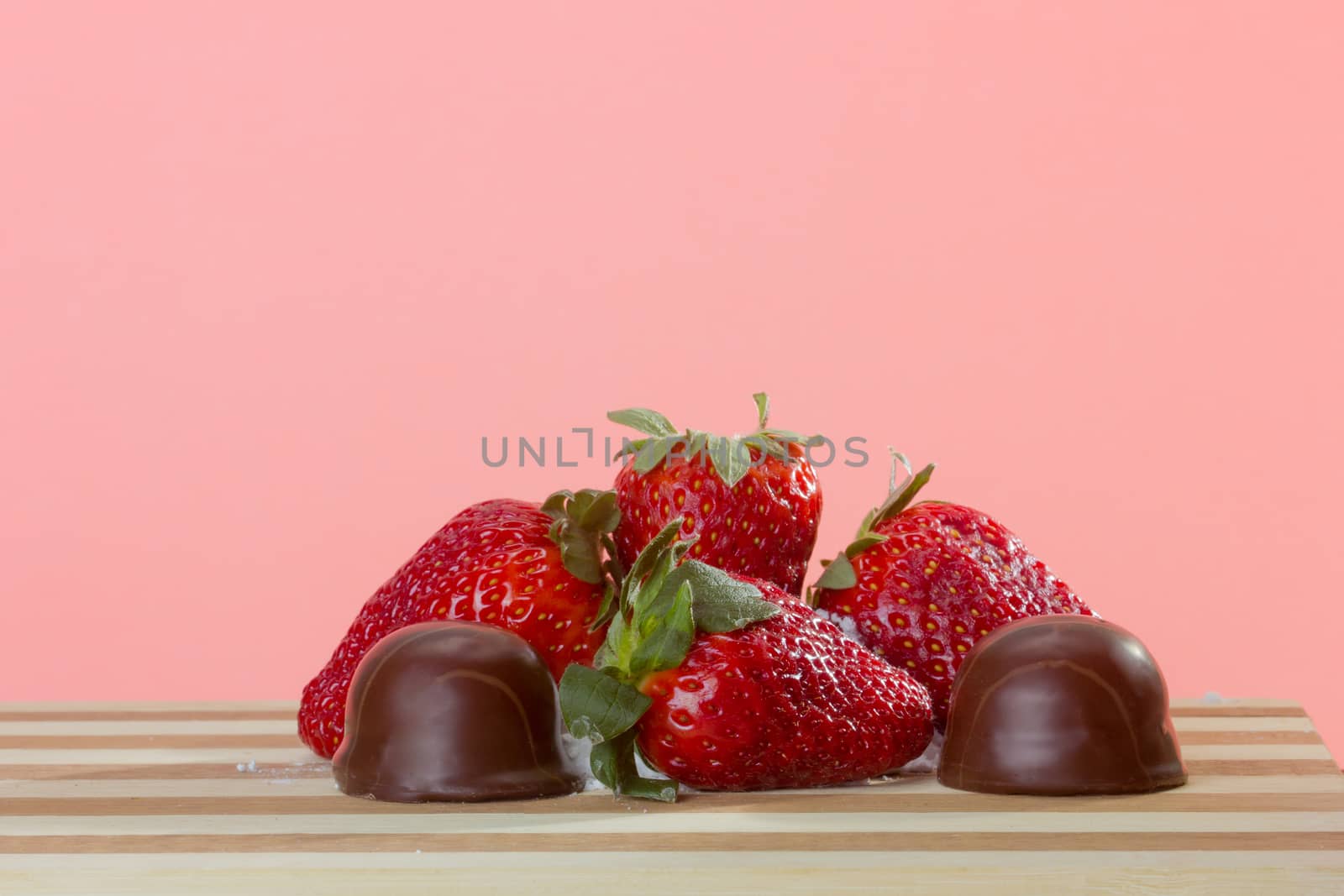 closeup of fresh strawberries and small chocolates on a wooden board