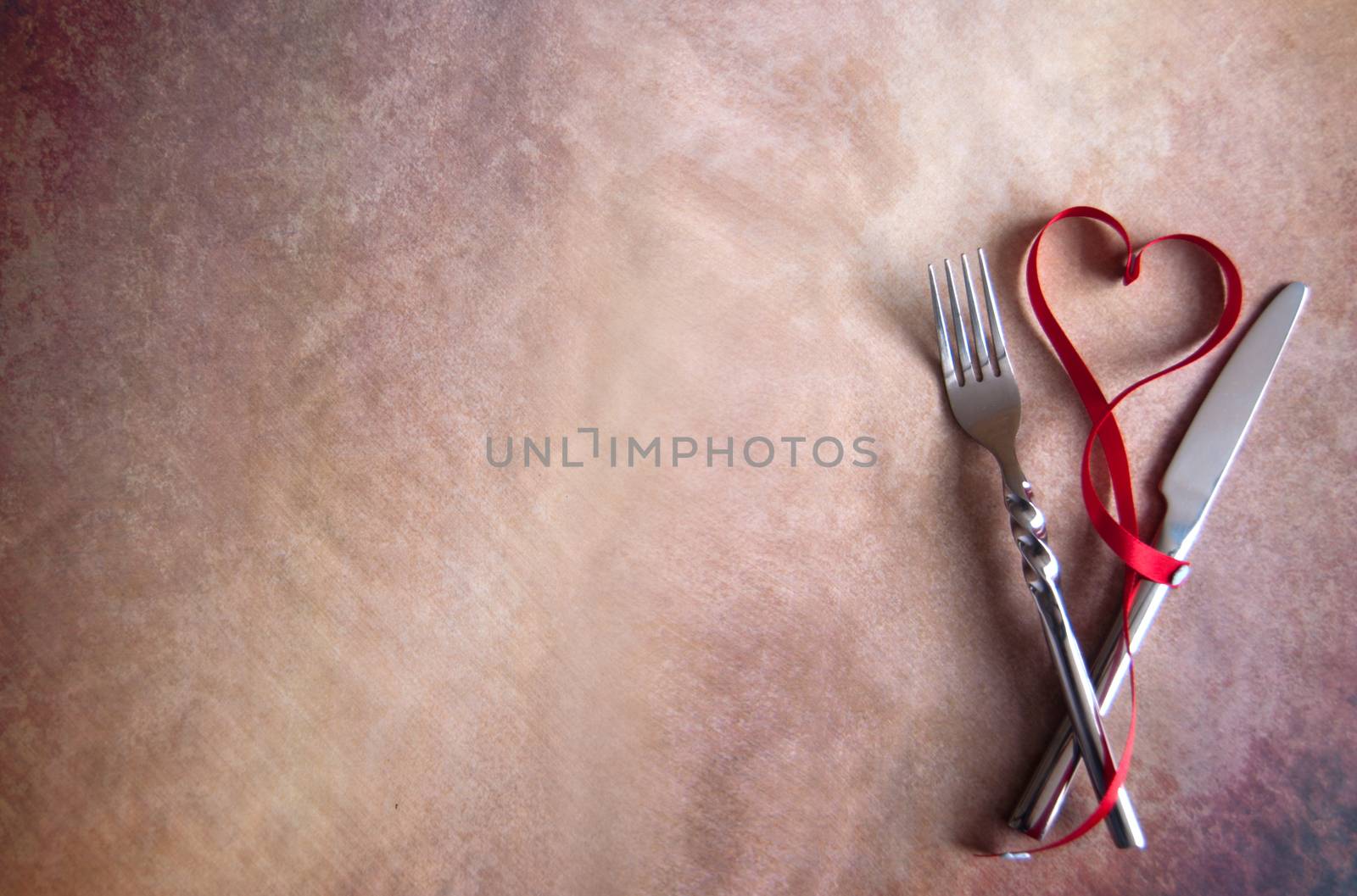 Red ribbon in the shape of a heart inbetween cutlery fork and knife