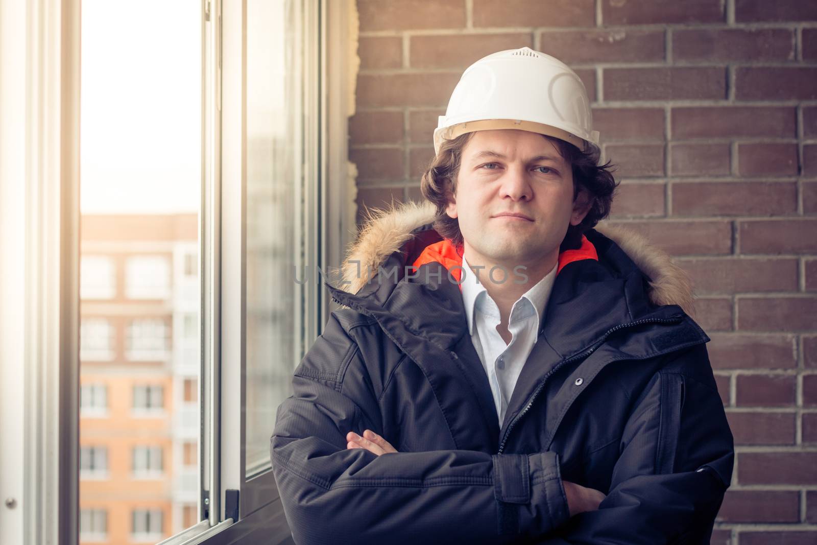 Portrait of engineer wear white safety helmet and cross his arms on construction site with brick background. Soft focus, toned