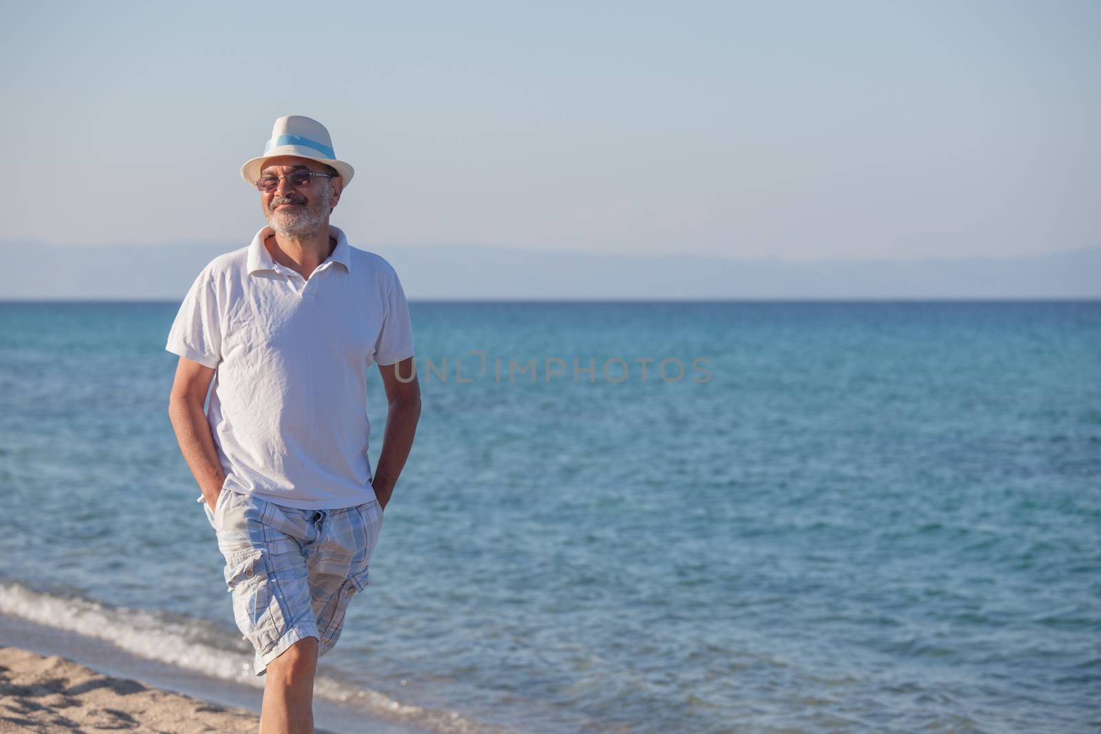 An elderly man is taking a walk on the beach in quiet summer afternoon.