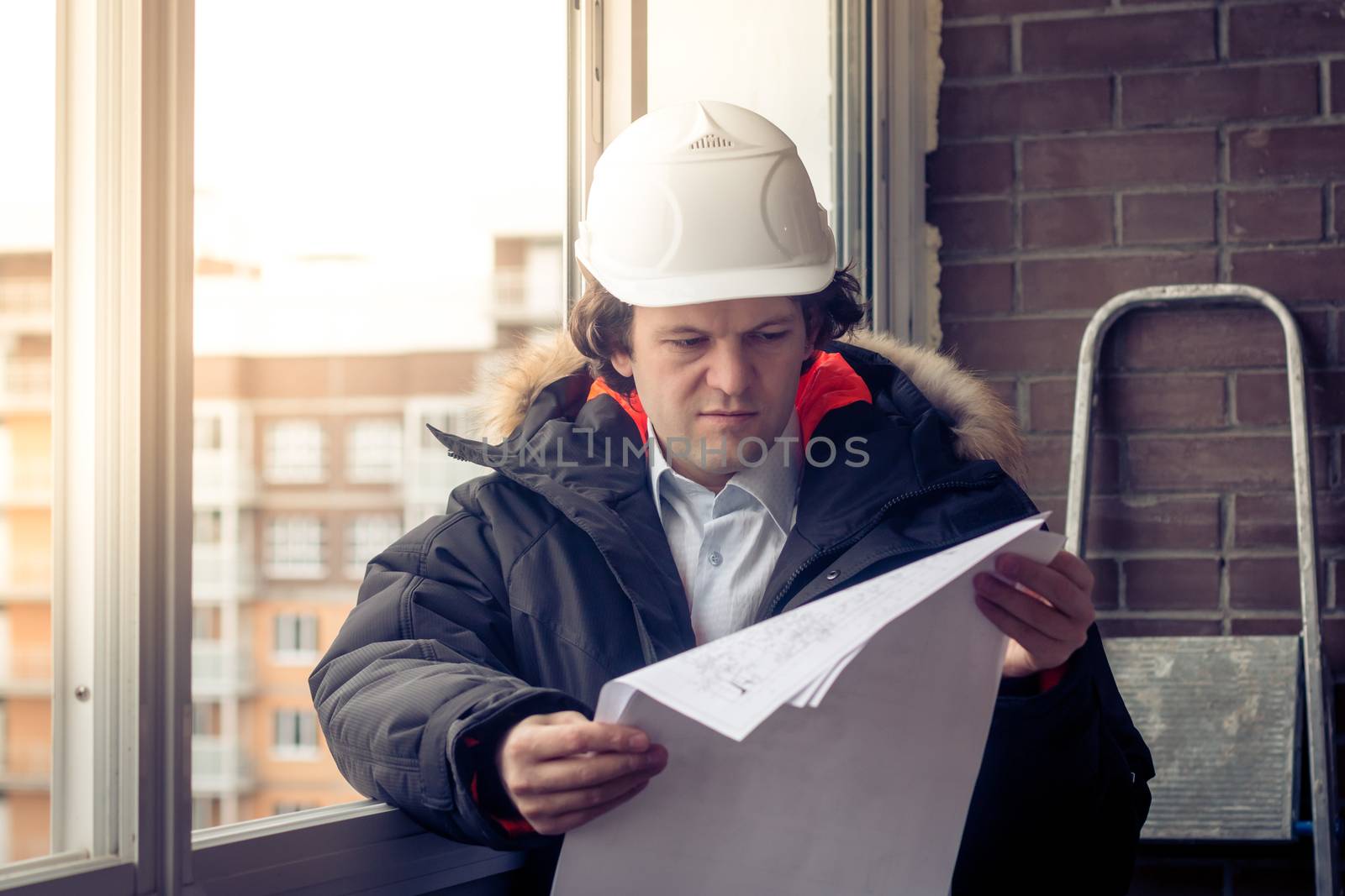 Working engineer in a white construction helmet with a project or drawing plan on the background of an industrial plant. Soft focus, toned