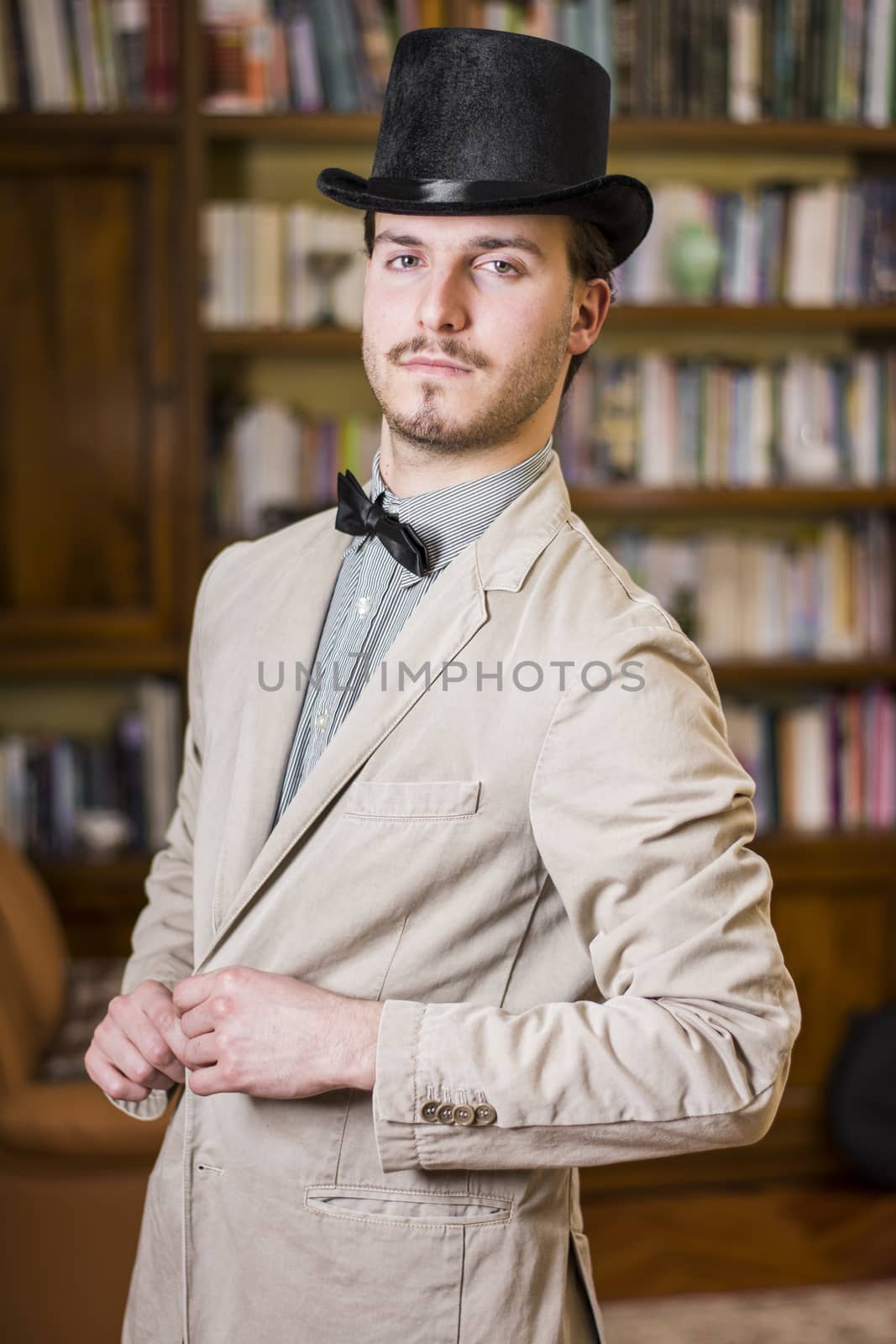 Attractive young man wearing top hat and bow tie, looking at camera. Indoors shot