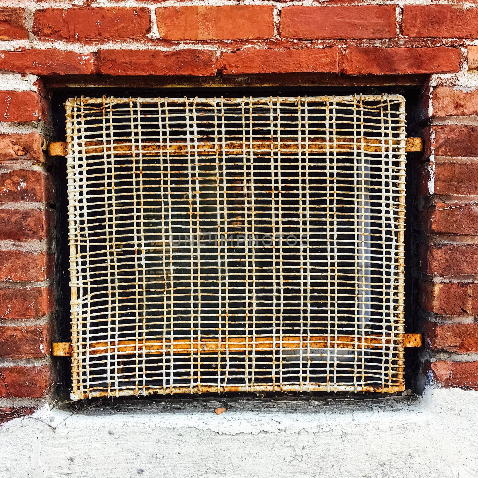 Old wire mesh protecting basement window of a red brick building.