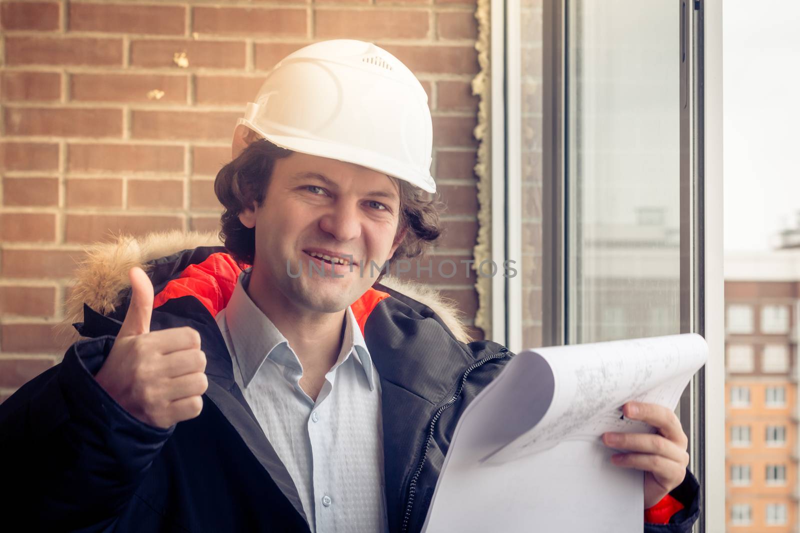 A construction worker giving his thumbs-up in front of a newly constructed residential building. Soft focus, toned