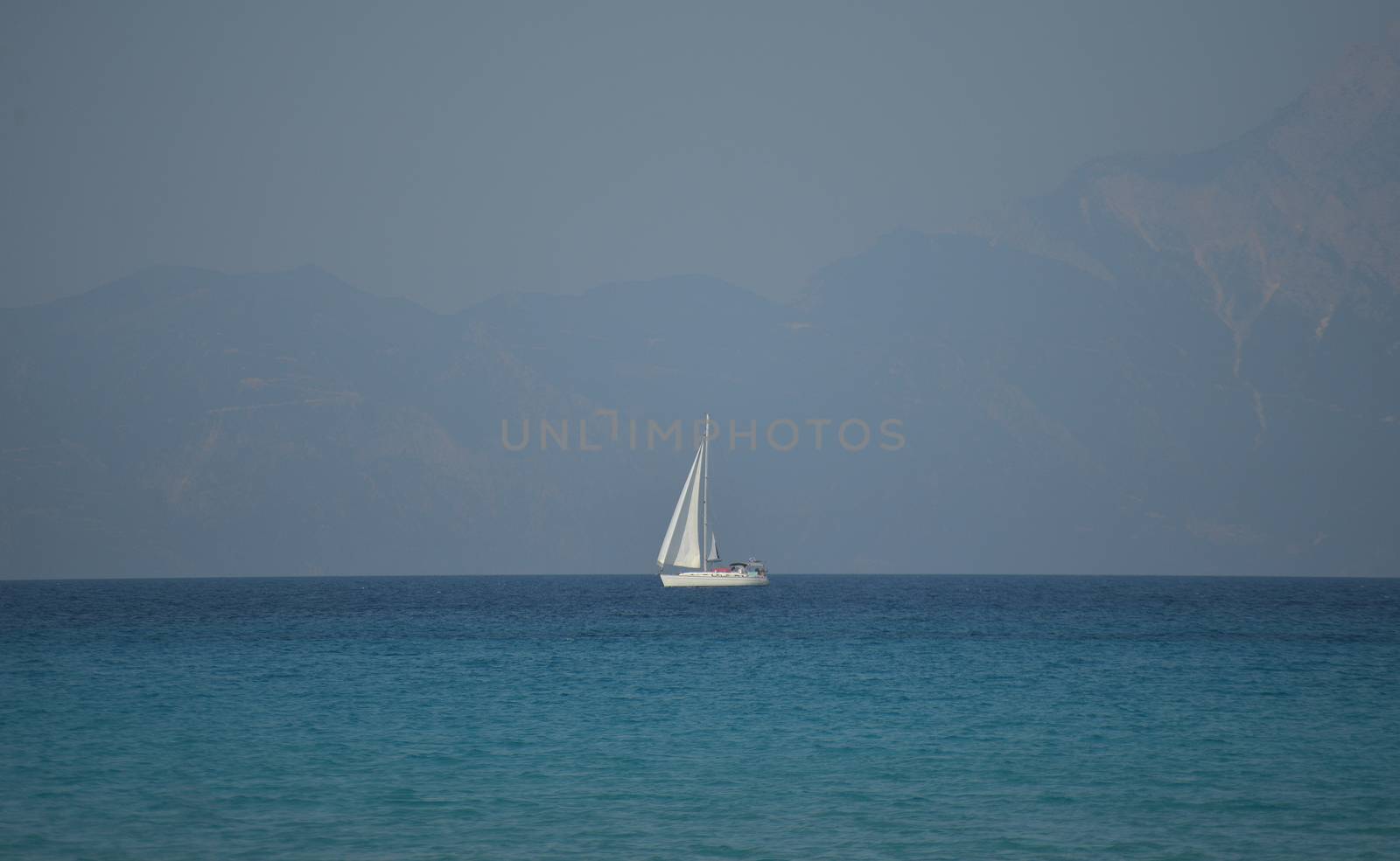 A white sailboat at sea in a hazy afternoon.