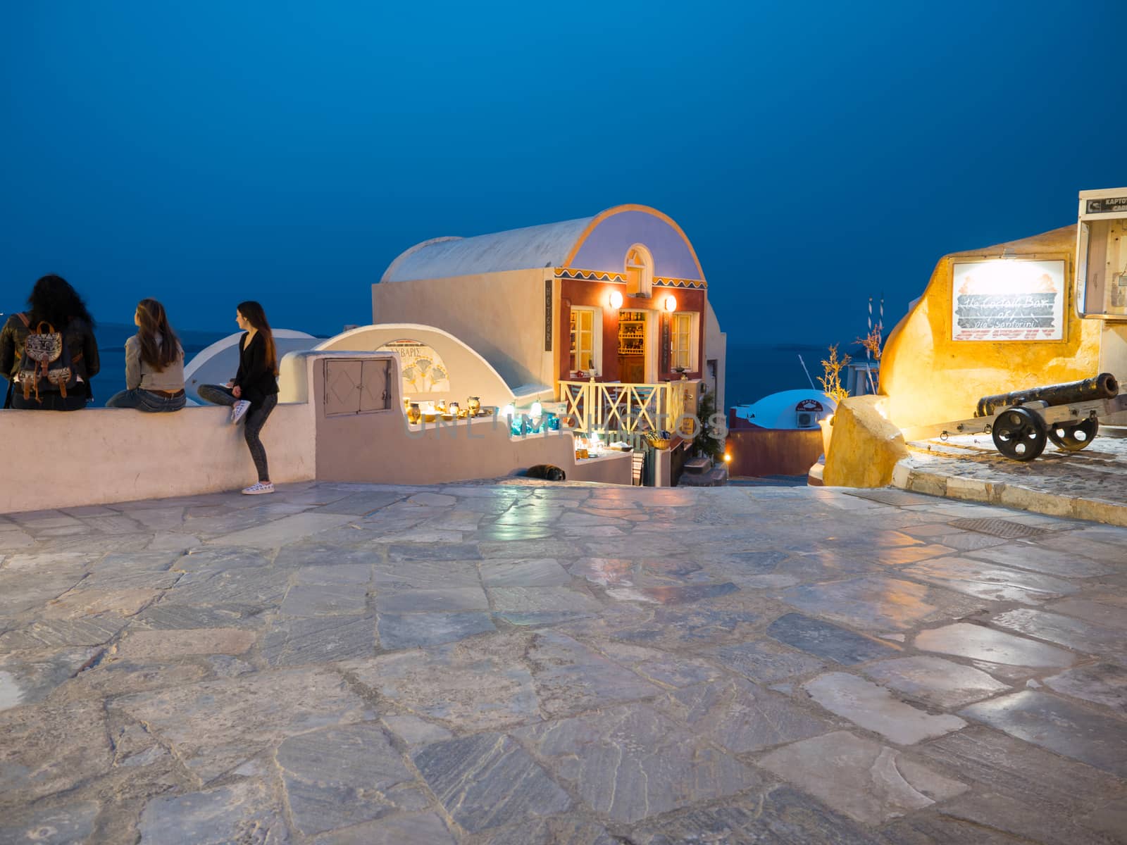 SANTORINI, GREECE - APRIL 7, 2017: Small square with lights and tourists enjoy the view late in the afternoon in Oia, Santorini island,Greece