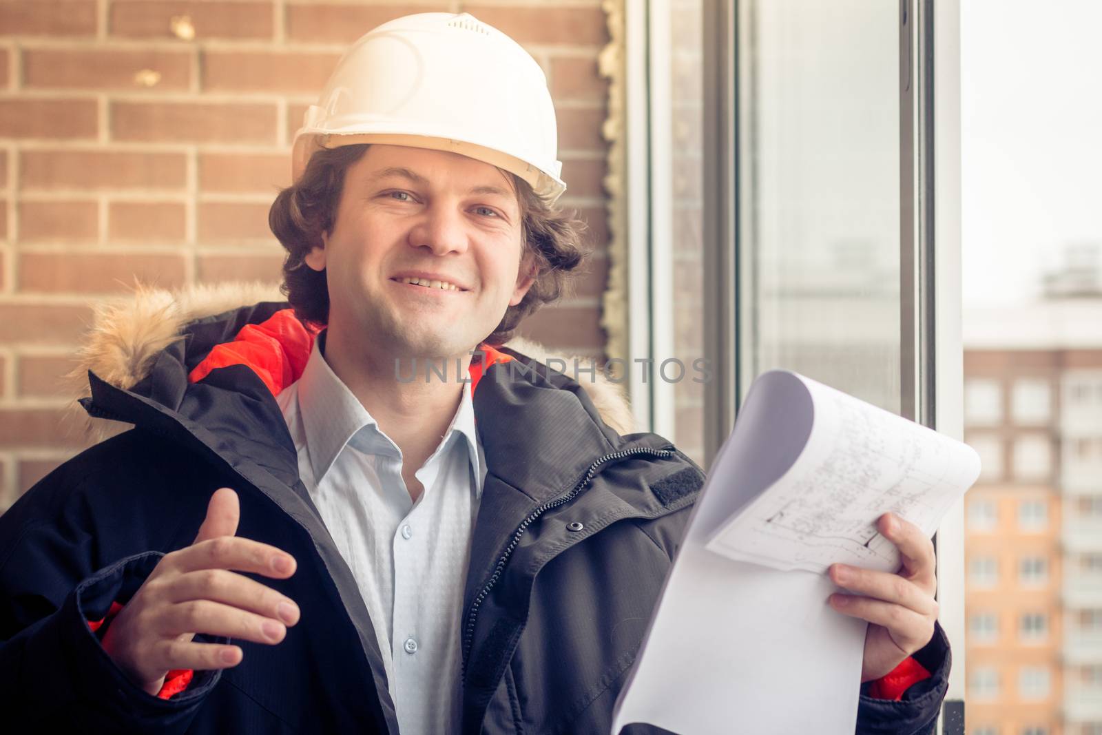 Portrait of cheerful young worker wearing hardhat posing looking at camera and smiling enjoying work on brick background. Soft focus, toned. by MSharova