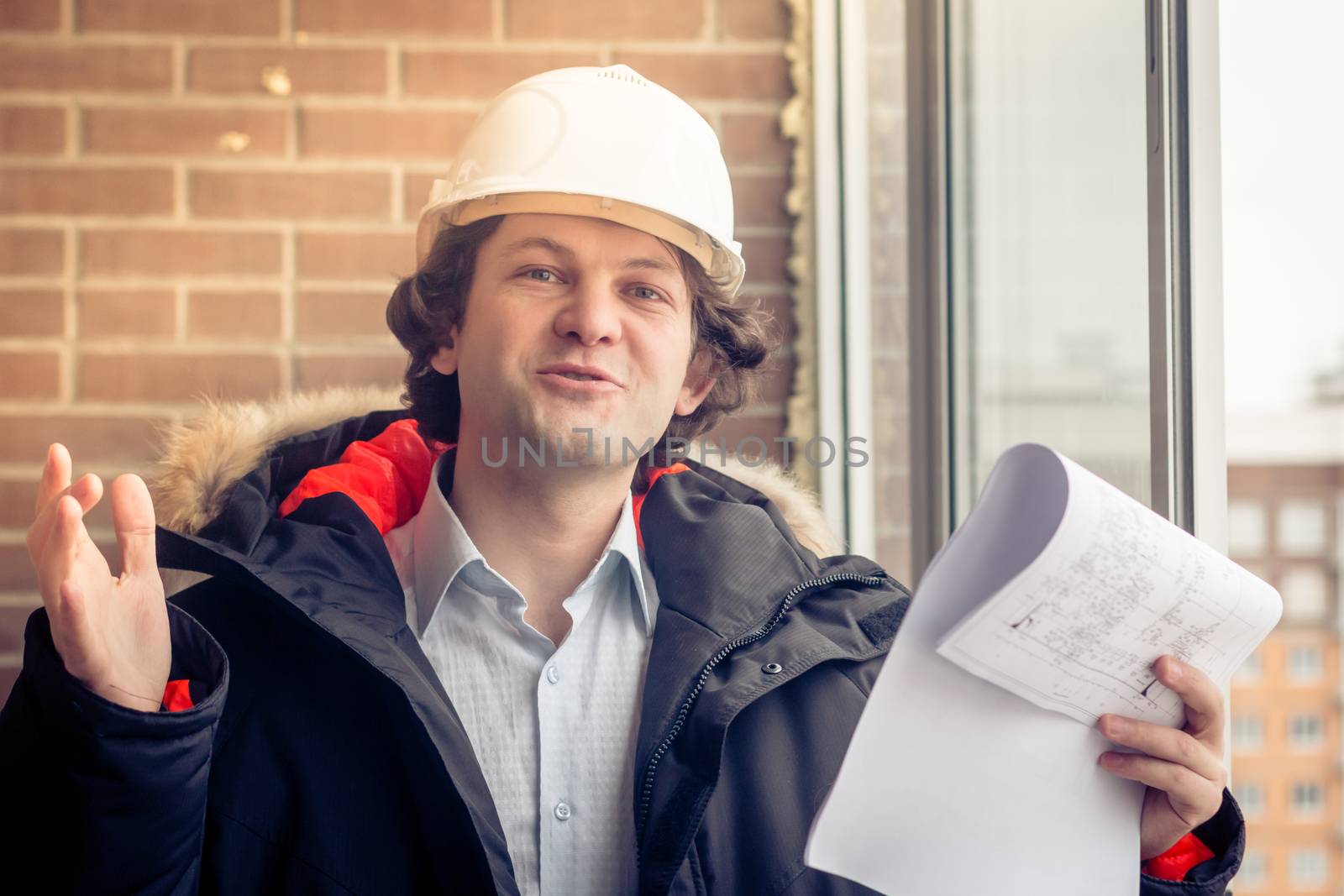 Portrait of cheerful young worker wearing hardhat posing looking at camera and smiling enjoying work on brick background. Soft focus, toned. by MSharova