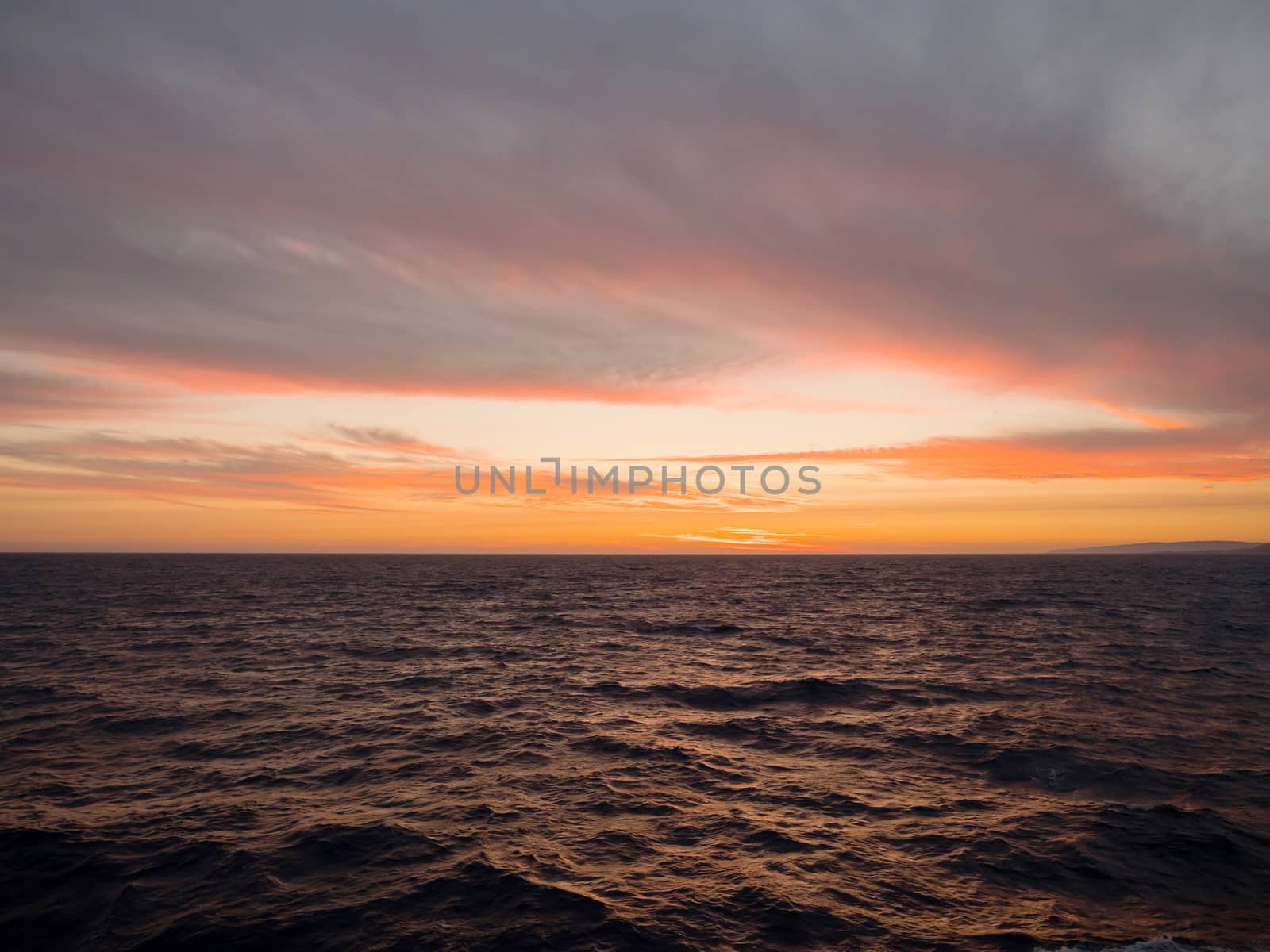 Sunset at the sea with deep orange colors in the afternoon and sky with clouds, view from a ship
