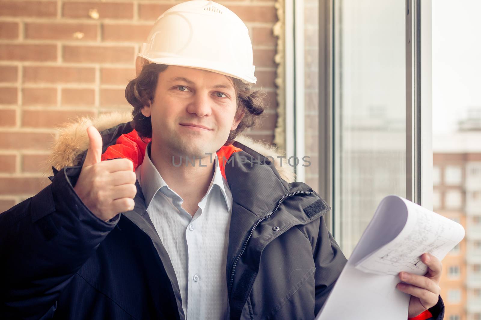 Attractive architect is giving thumb up. The man is smiling and looking at the camera with happiness. His plan was approved. Soft focus, toned