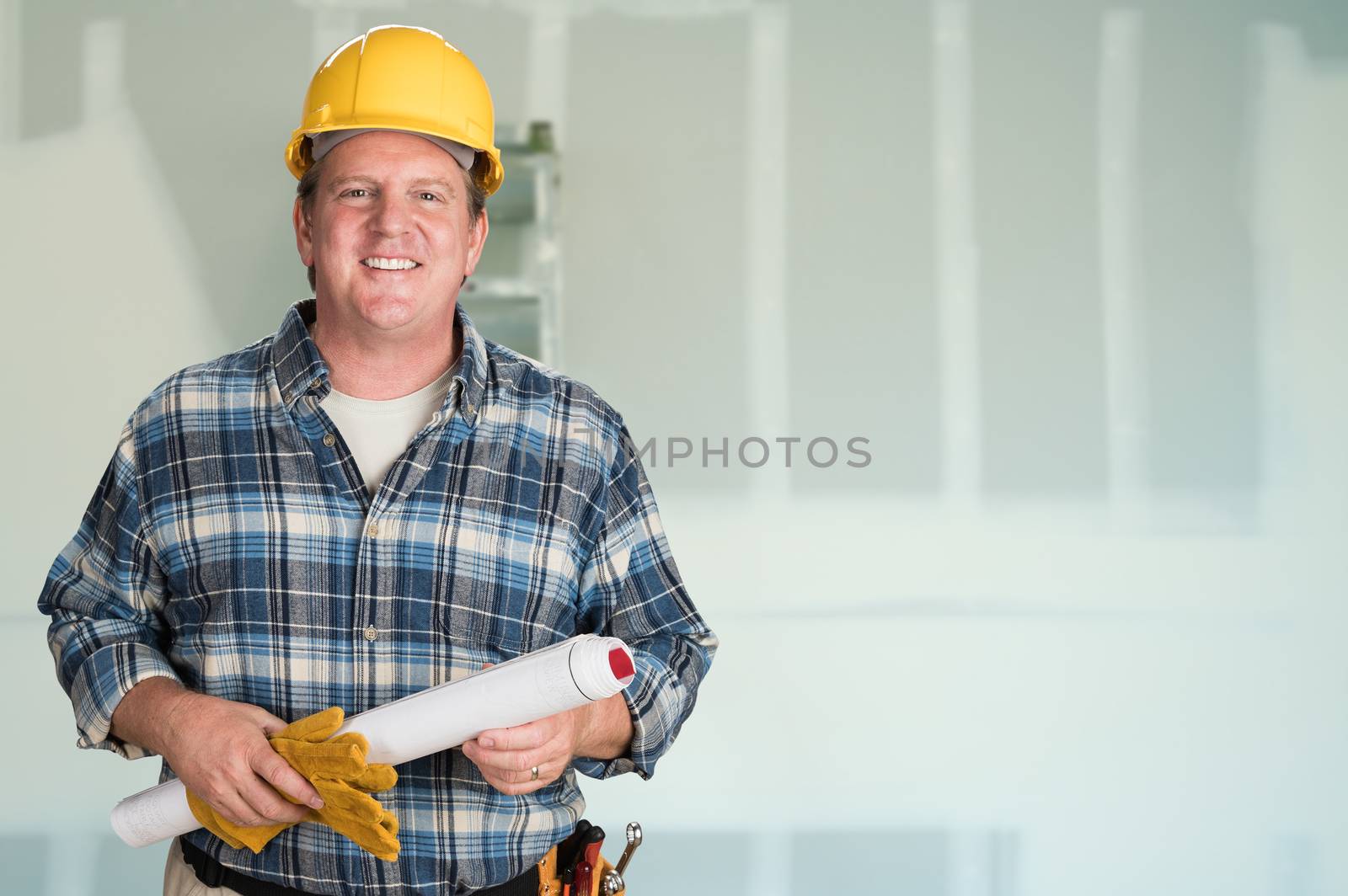 Contractor with Plans and Hard Hat In Front of Drywall. by Feverpitched