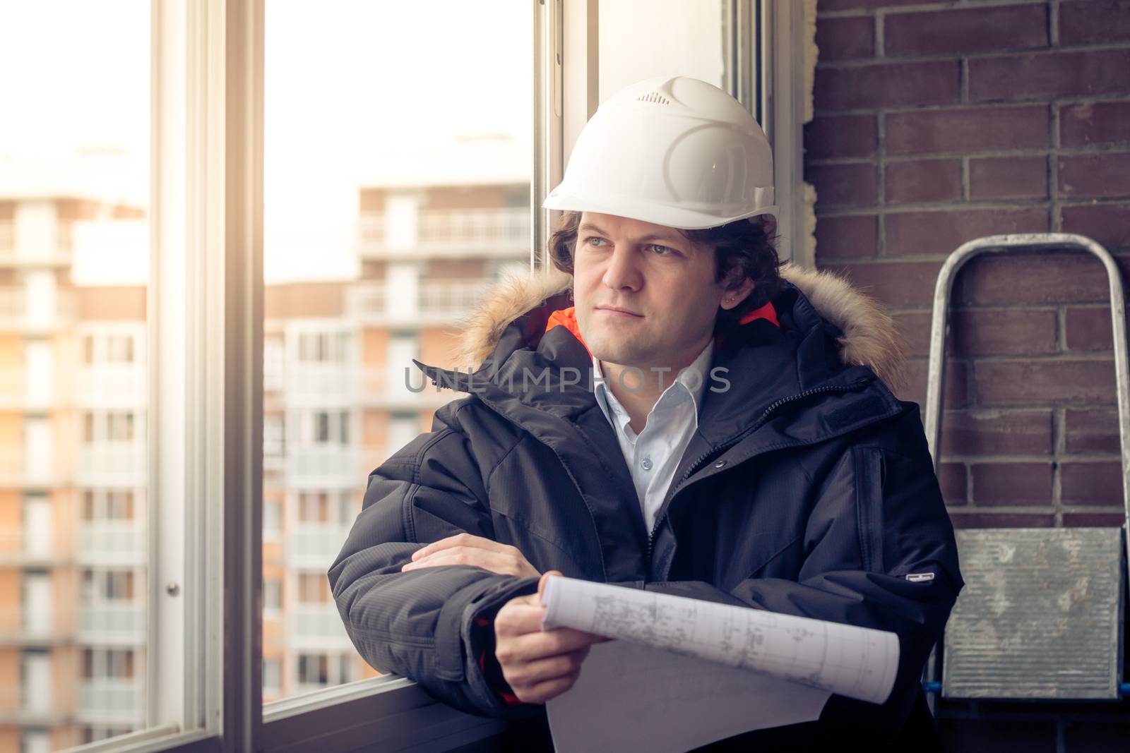 Pensive young man builder in hard hat standng and thinking. Soft focus, toned