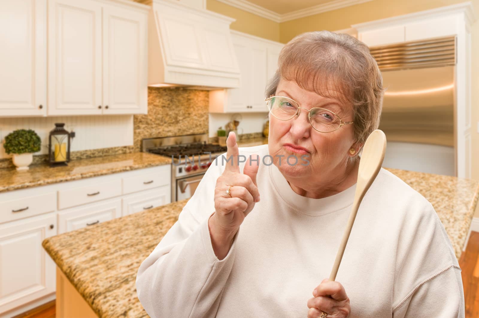 Senior Adult Woman Scolding with The Wooden Spoon Inside Kitchen by Feverpitched