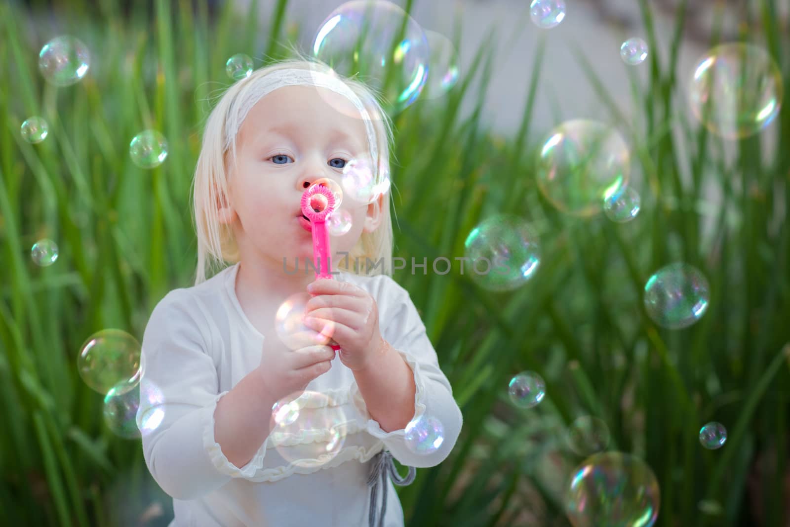 Adorable Little Girl Sitting On Bench Having Fun With Blowing Bubbles Outside. by Feverpitched