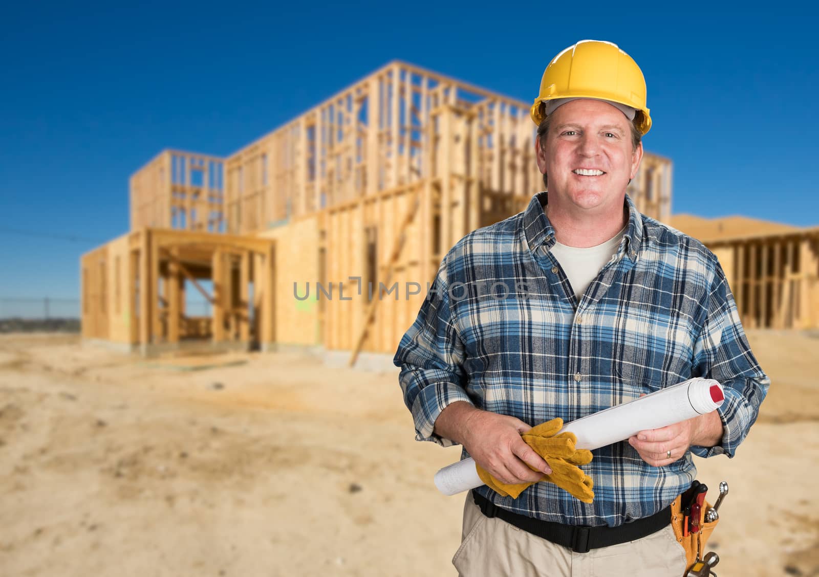 Contractor with Plans and Hard Hat In Front of New House Framing at Construction Site. by Feverpitched