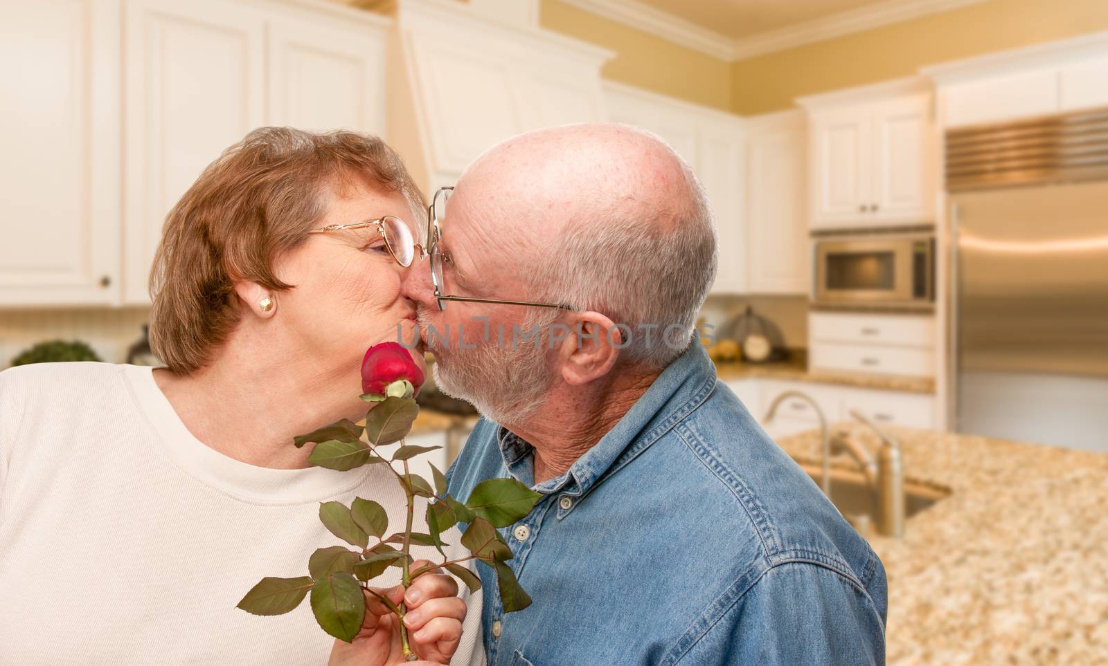 Happy Senior Adult Man Giving Red Rose to His Wife Inside Kitchen. by Feverpitched