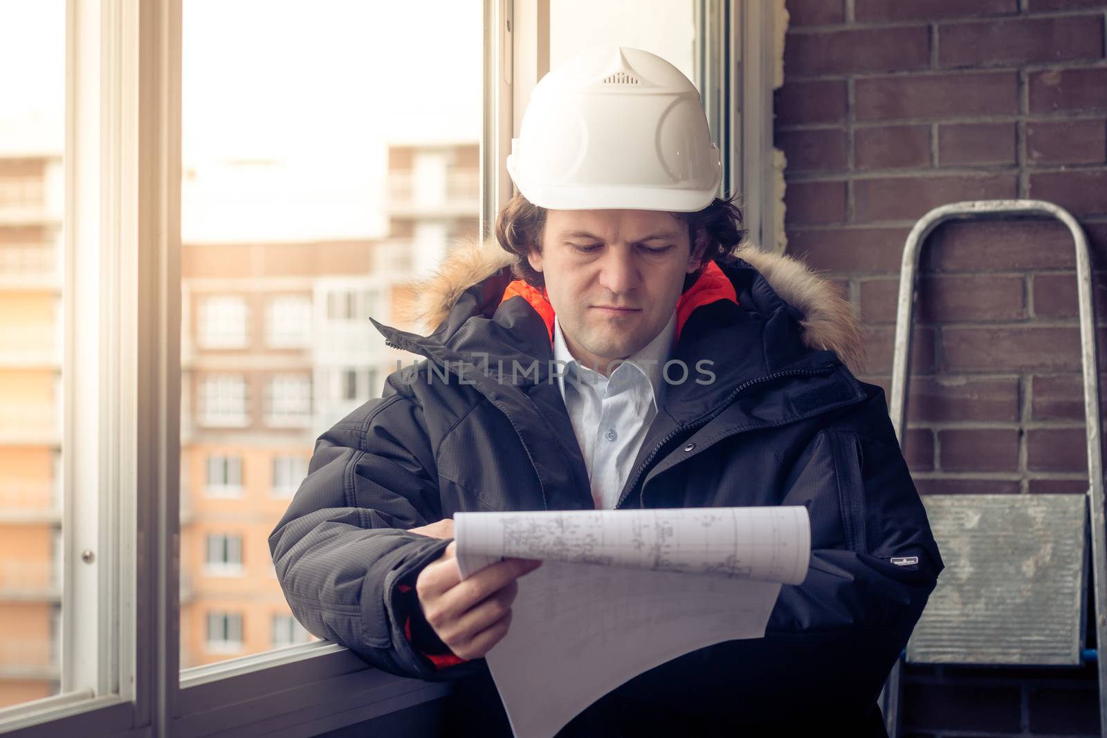 Engineer-builder working with documents on the construction site. Worker inspects drawings on the construction site against the background of brick wall. Soft focus, toned
