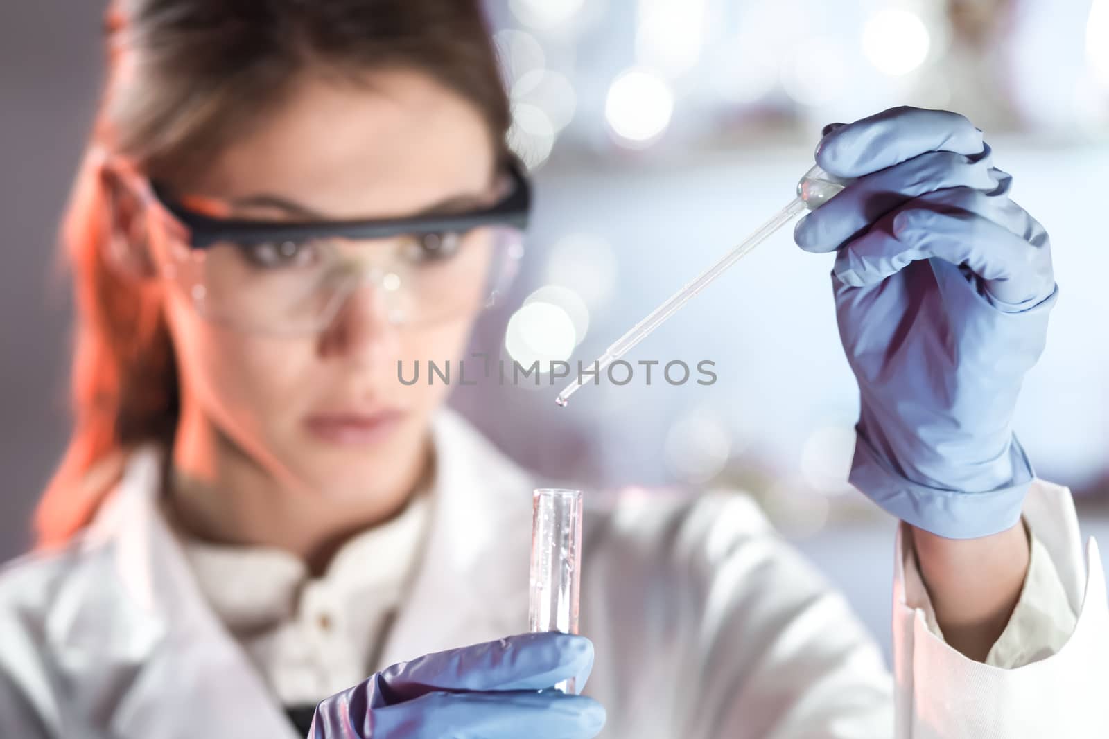 Life scientists researching in laboratory. Focused female life science professional pipetting solution into the glass cuvette. Lens focus on researcher's eyes. Healthcare and biotechnology concept.
