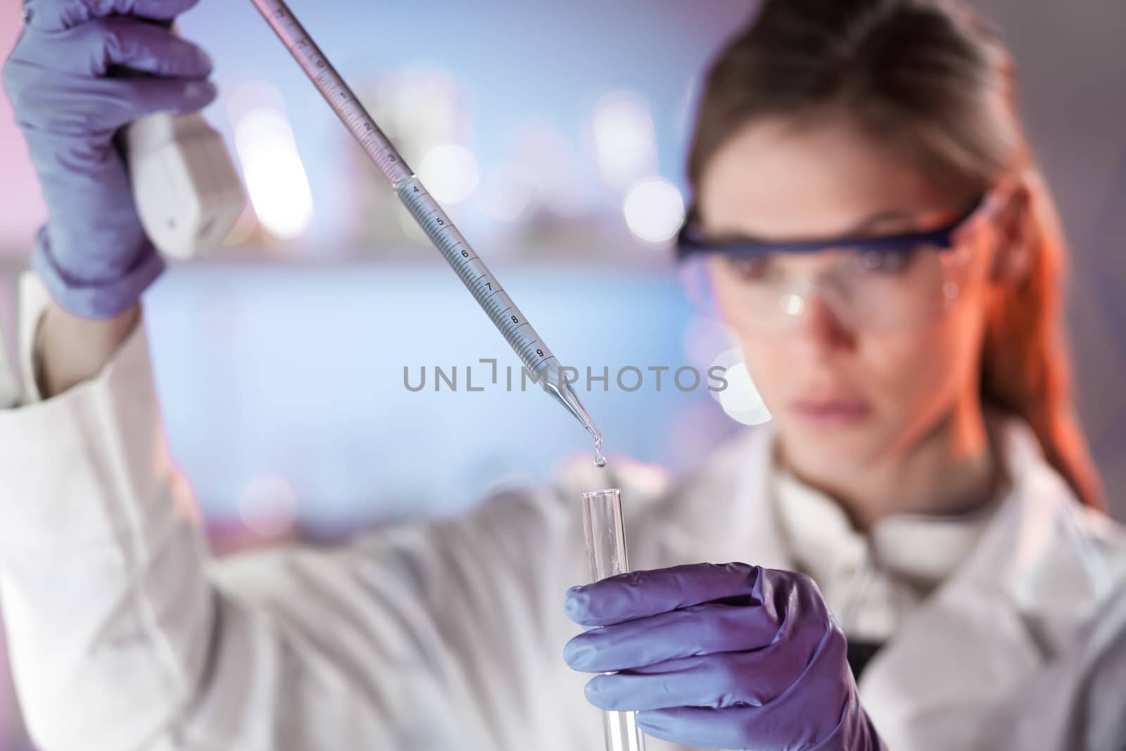 Life scientists researching in laboratory. Focused female life science professional pipetting solution into the glass cuvette. Lens focus on researcher's eyes. Healthcare and biotechnology concept.