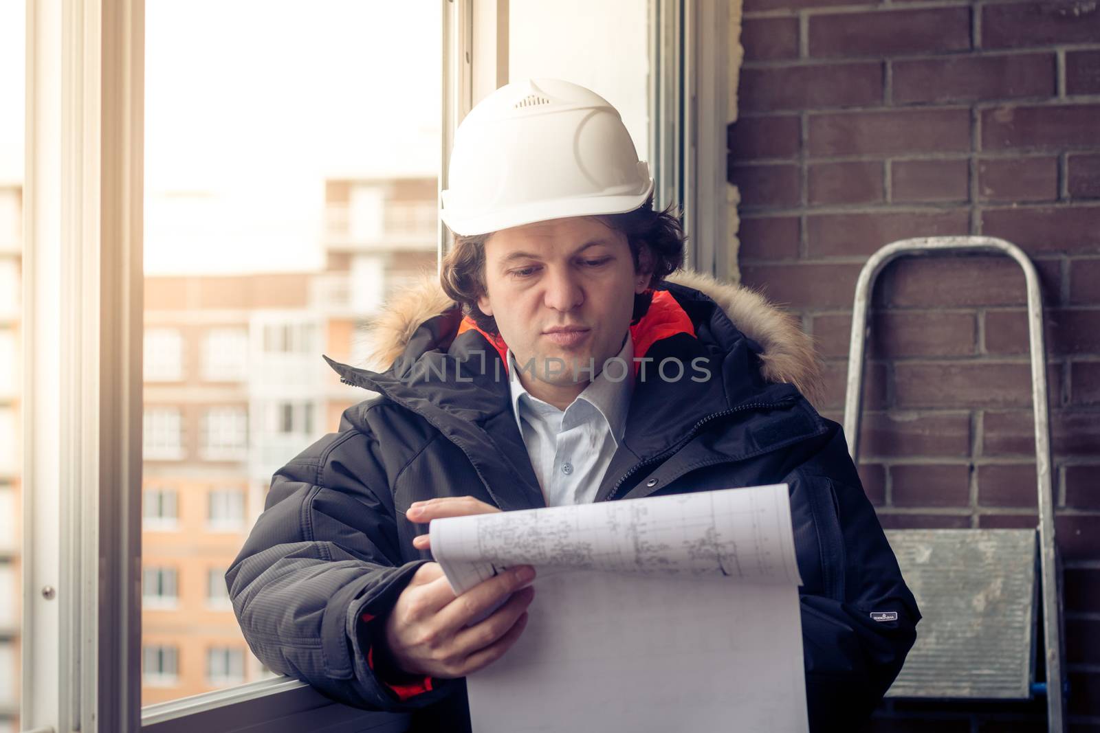 Engineer-builder working with documents on the construction site. Worker inspects drawings on the construction site against the background of brick wall. Soft focus, toned