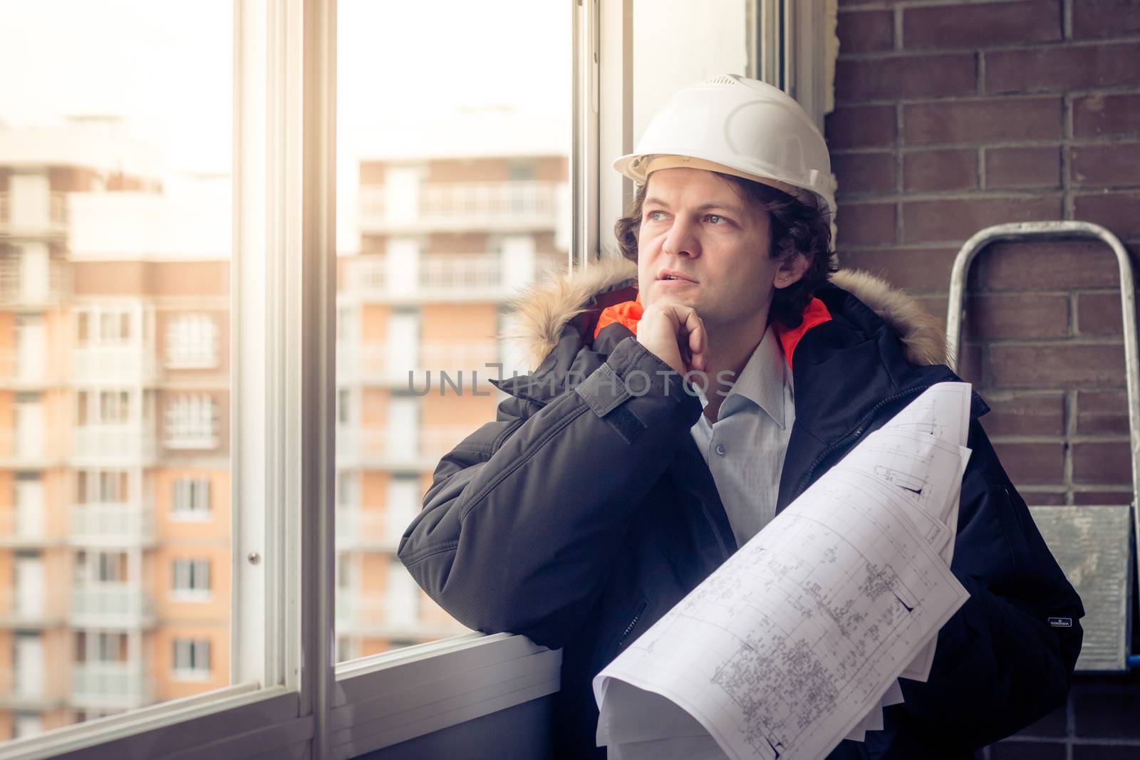 Pensive young man builder in hard hat standng and thinking. Soft focus, toned. by MSharova