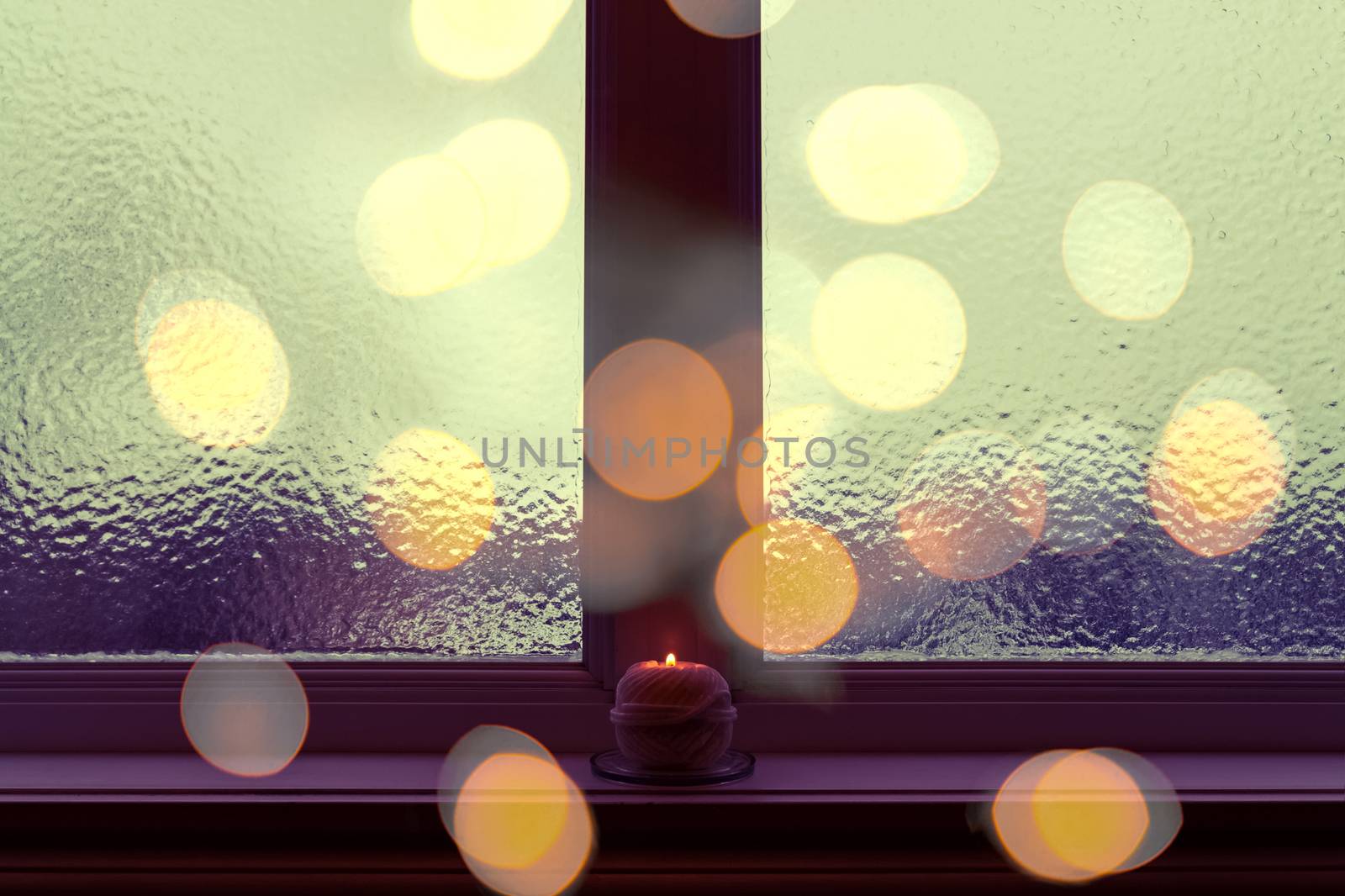 Frosted window in dark evening light, with a candle burning on a windowsill.