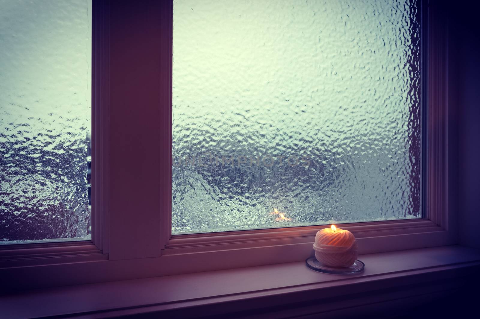 Candle burning near a frosted window in twilight by anikasalsera